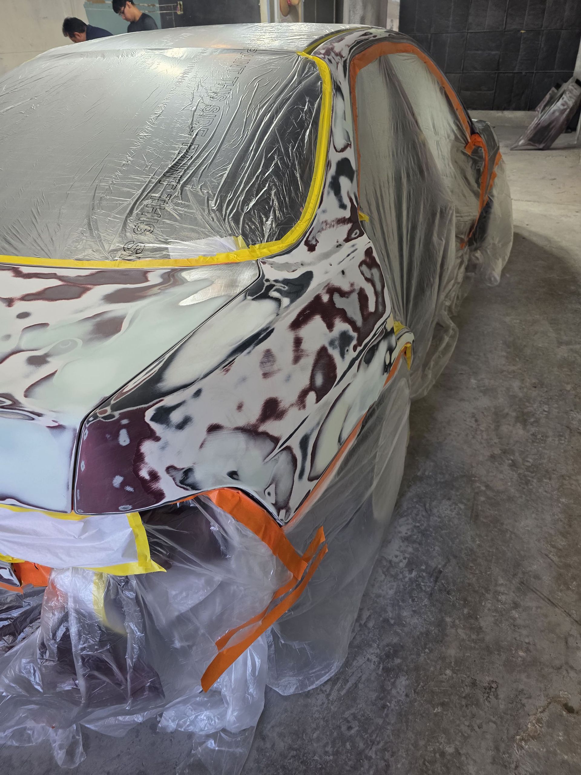 Car covered in masking tape and plastic at a body shop, mid-paint preparation