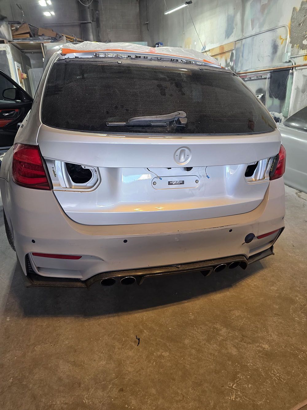 Silver SUV with rear bumper damage, parked in a wet indoor auto repair bay