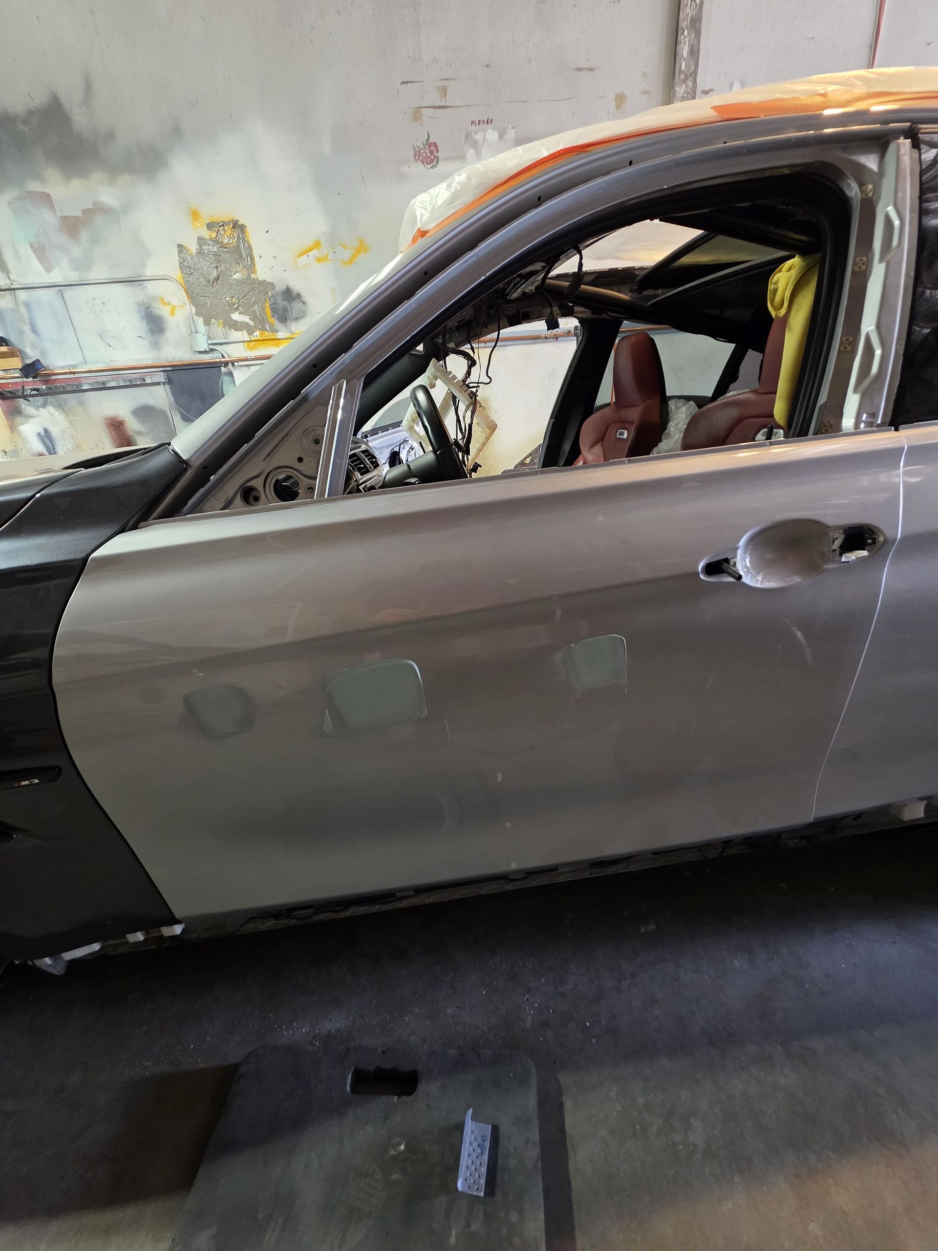 Damaged gray sedan in a workshop, side view with missing window glass and interior exposed