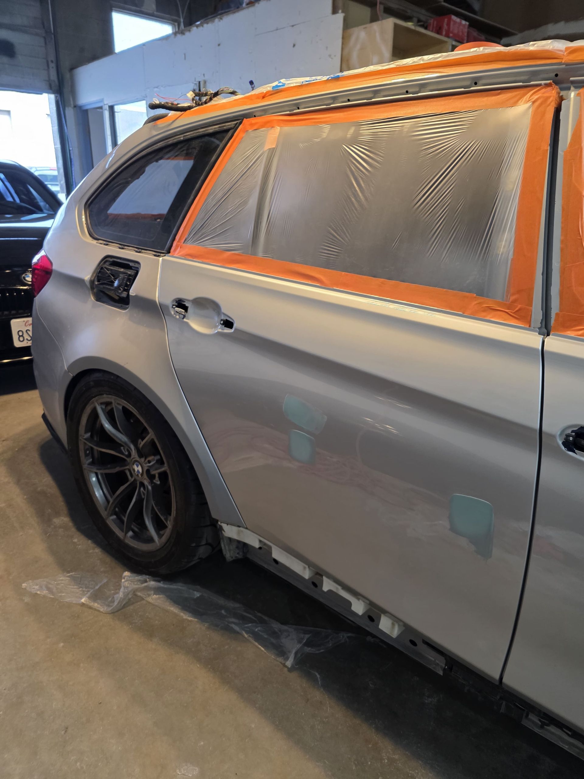 Gray hatchback car in a garage, rear side covered with orange tape and protective plastic over windows