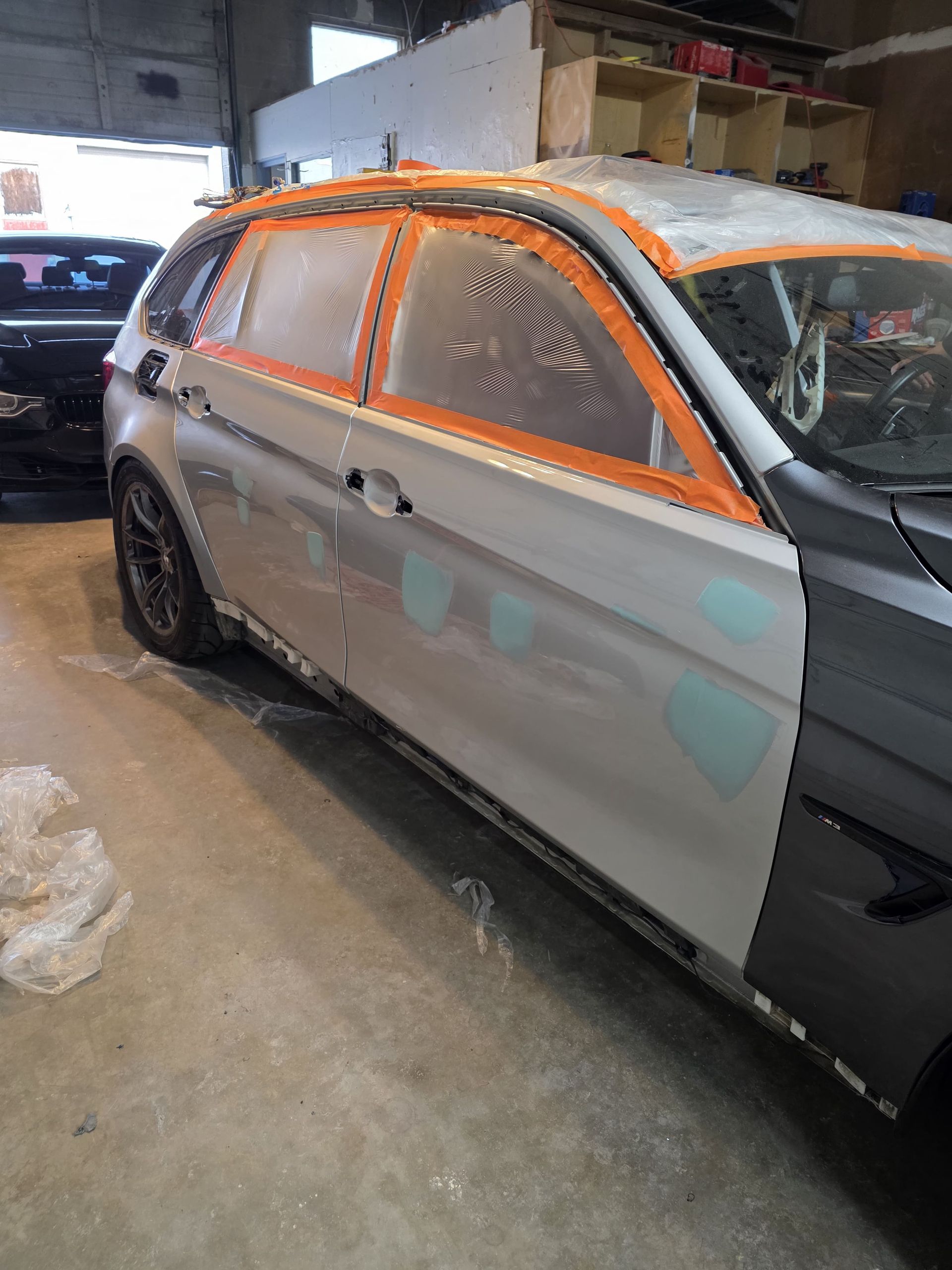 Partially repaired silver SUV in an auto body shop, with orange masking tape around windows and roof.