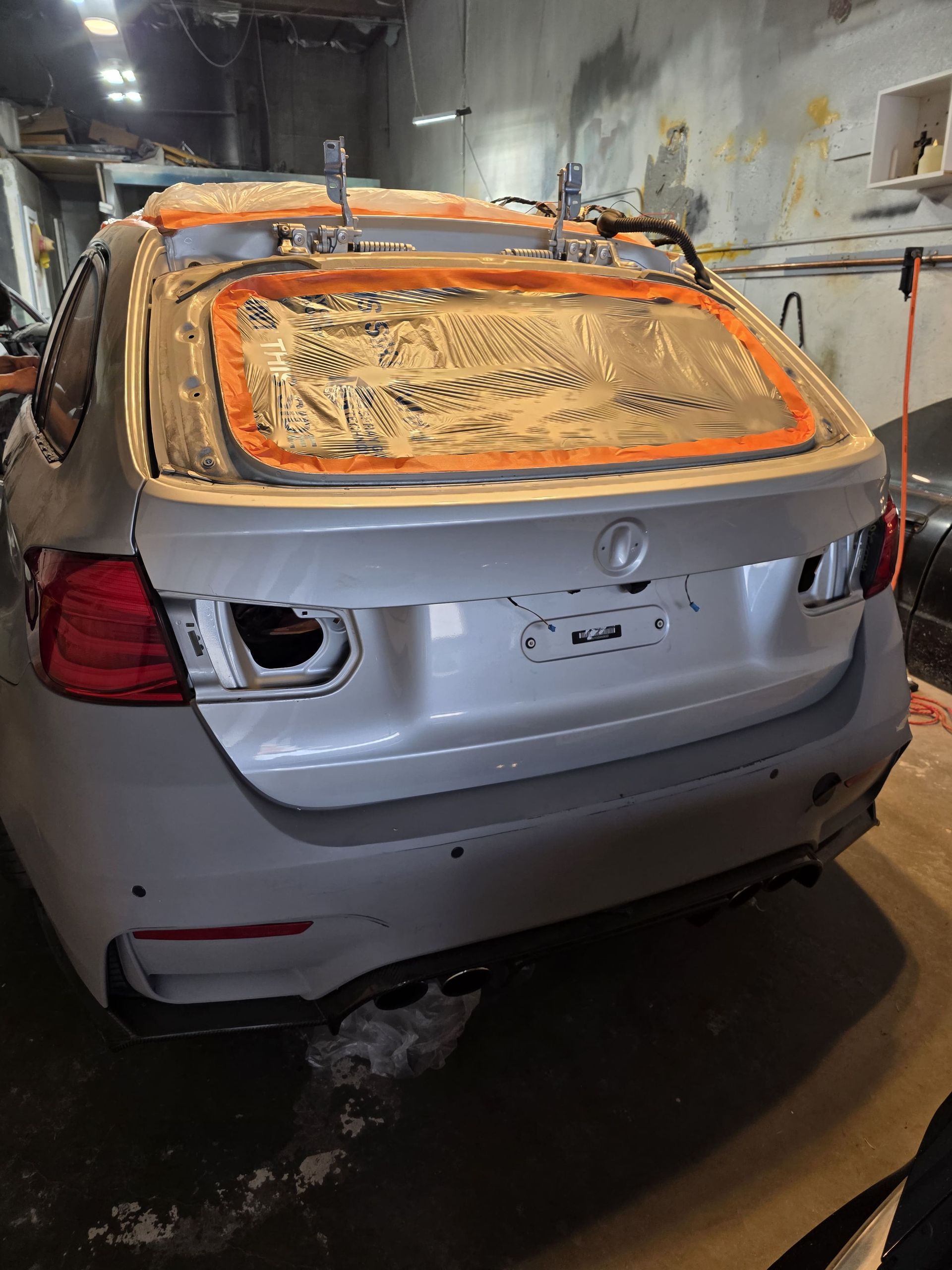 Silver SUV with rear window covered in orange insulation foam inside a garage, rear damage visible