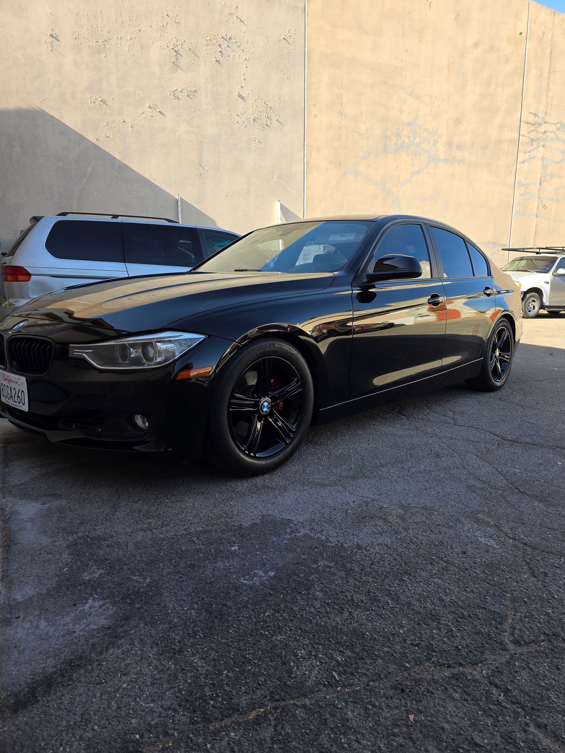 Black sedan parked outdoors beside a white car against a beige wall.