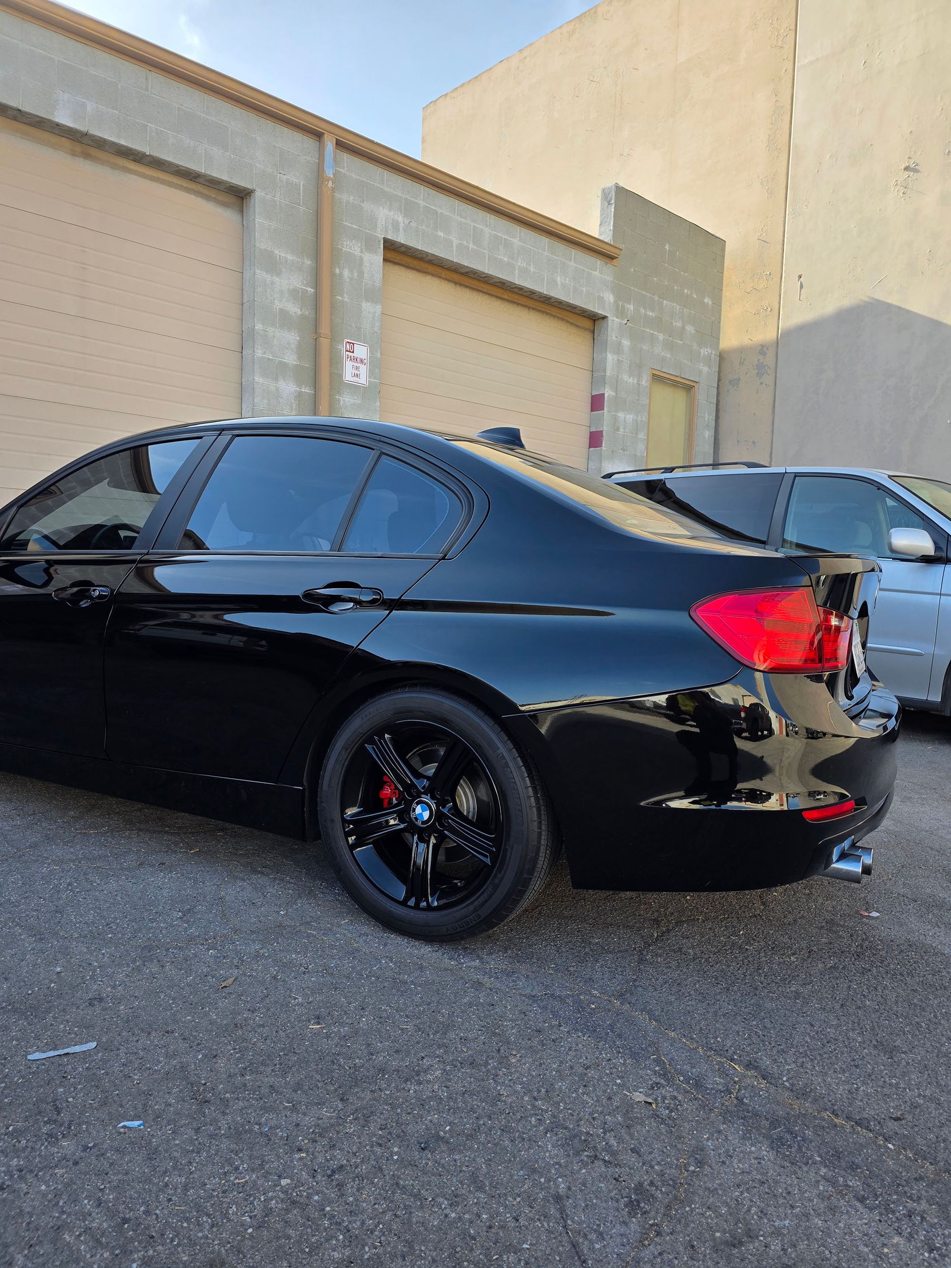 Black sedan with tinted windows parked beside beige buildings in a lot