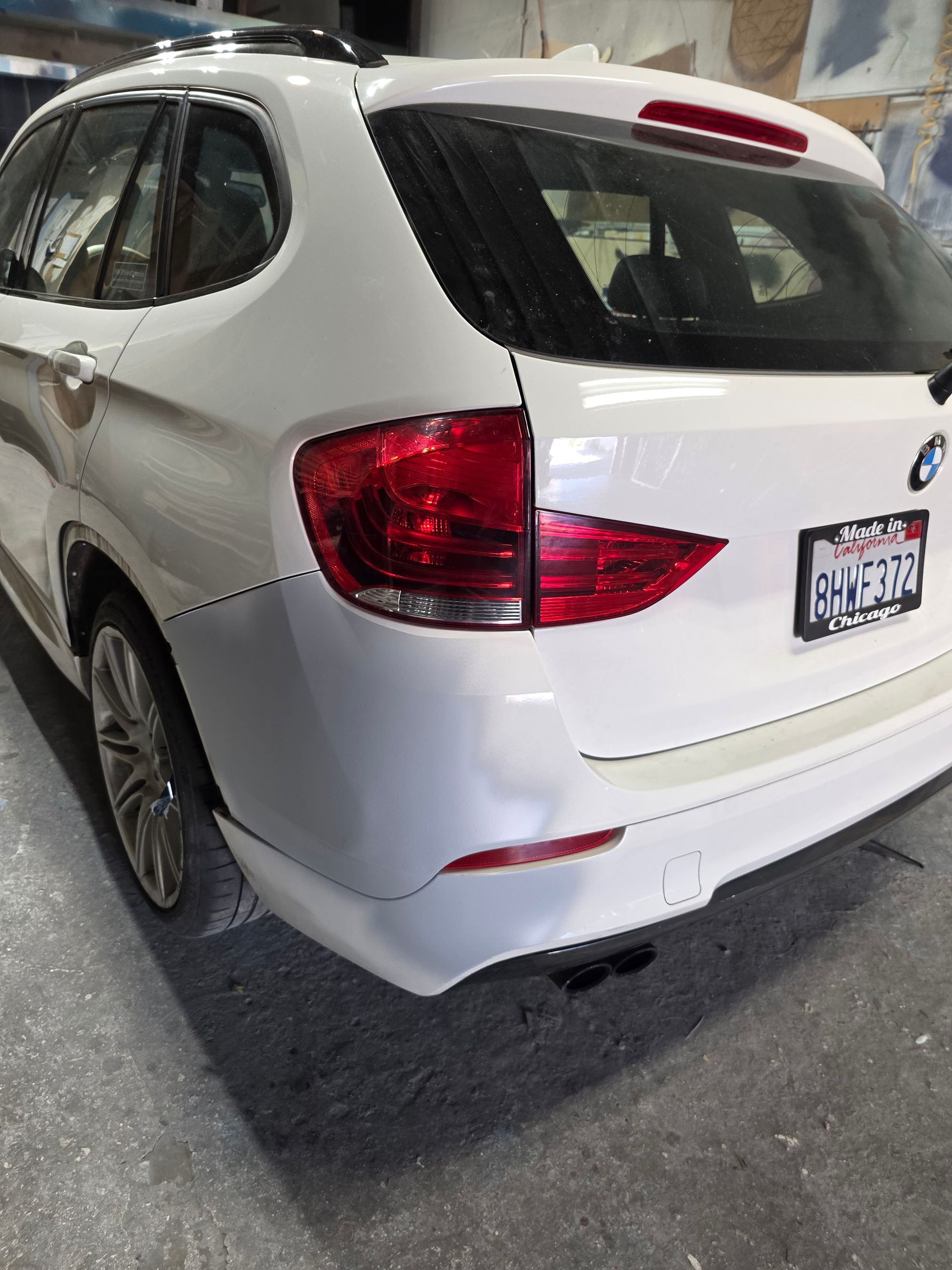 White SUV parked in a garage, rear-left view with red taillights and dented rear bumper