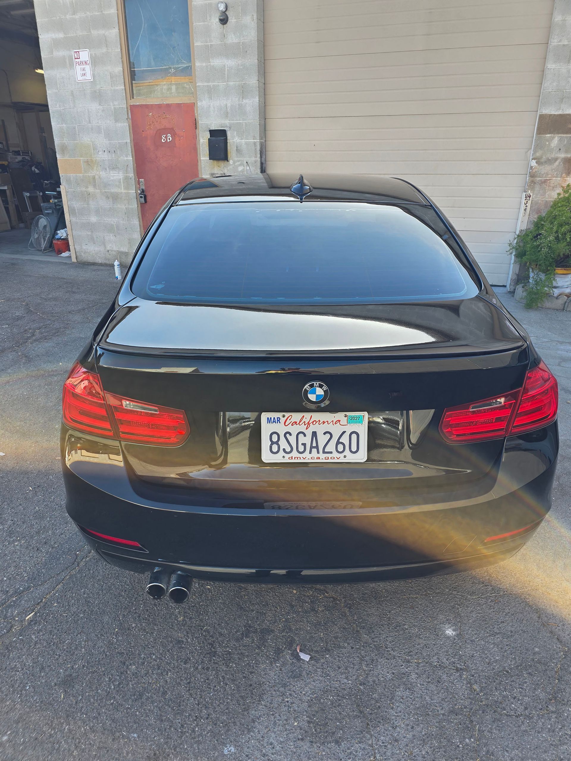 Black sedan parked in front of a garage, rear view with California license plate.