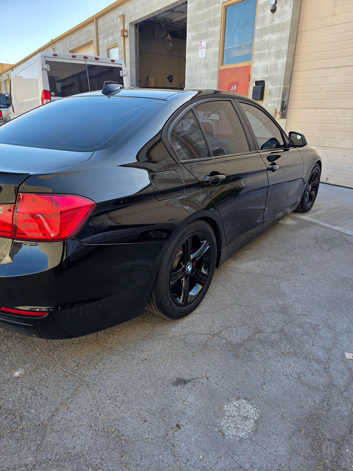 Black sedan parked beside an industrial warehouse, viewed from the rear-left side.