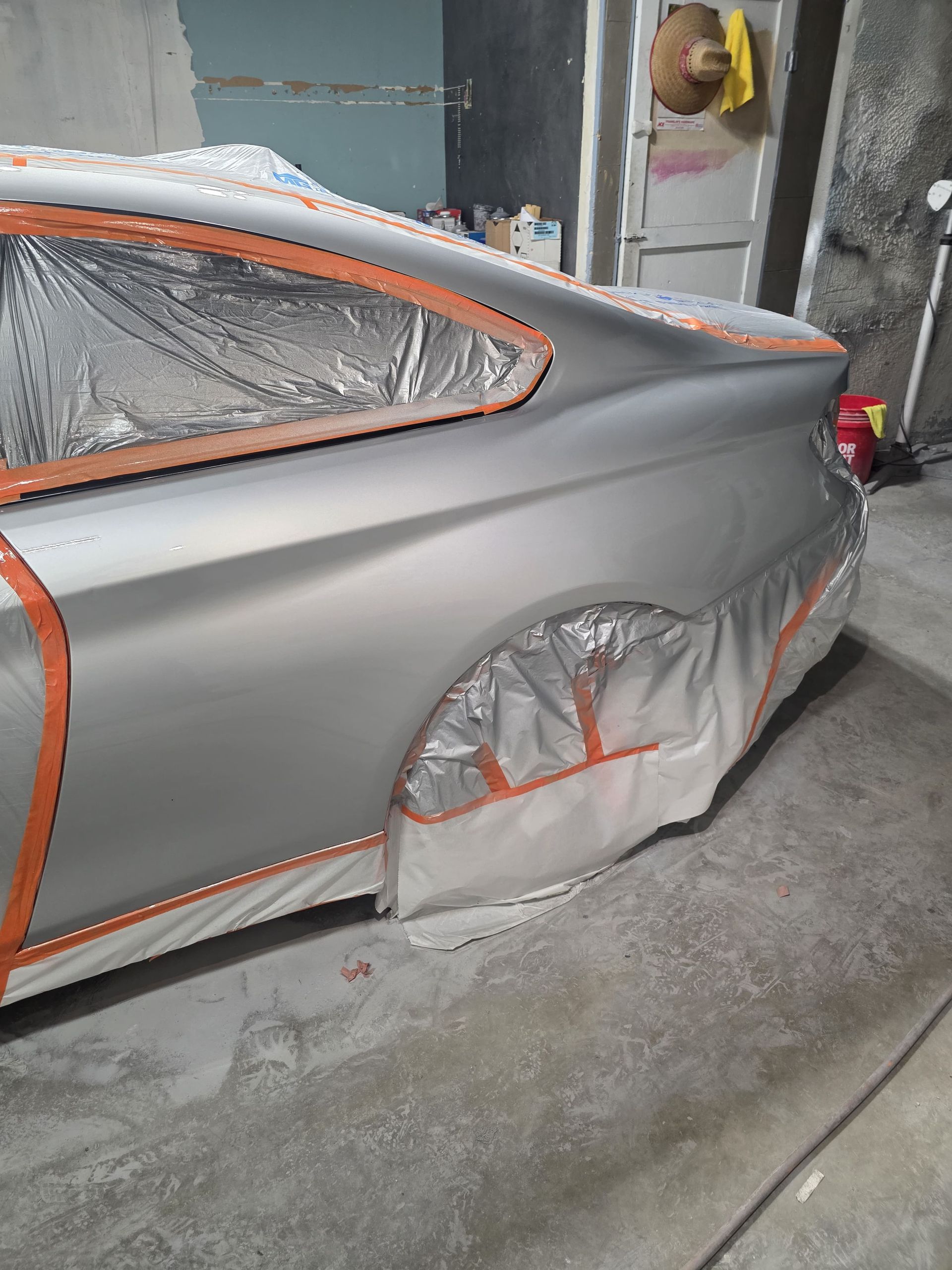 Silver car in auto body shop, masked with tape and plastic for painting or repair