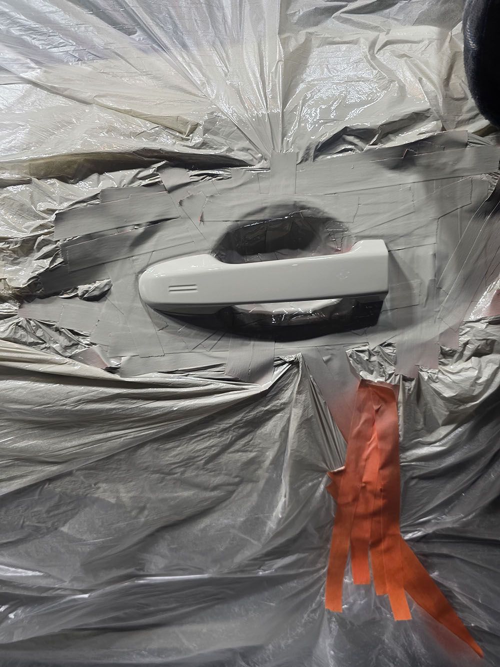 White car door handle on a car wrapped in gray plastic, with orange tape below
