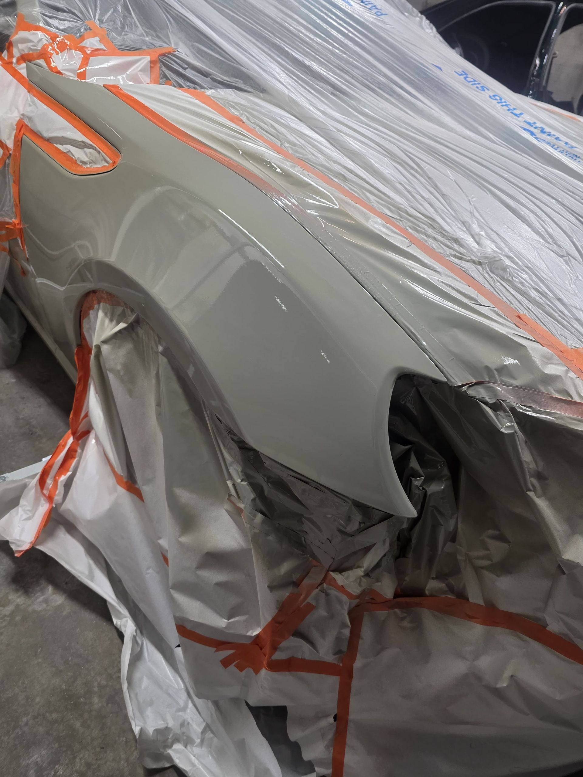 Gray car covered in masking plastic and tape during auto body paint preparation