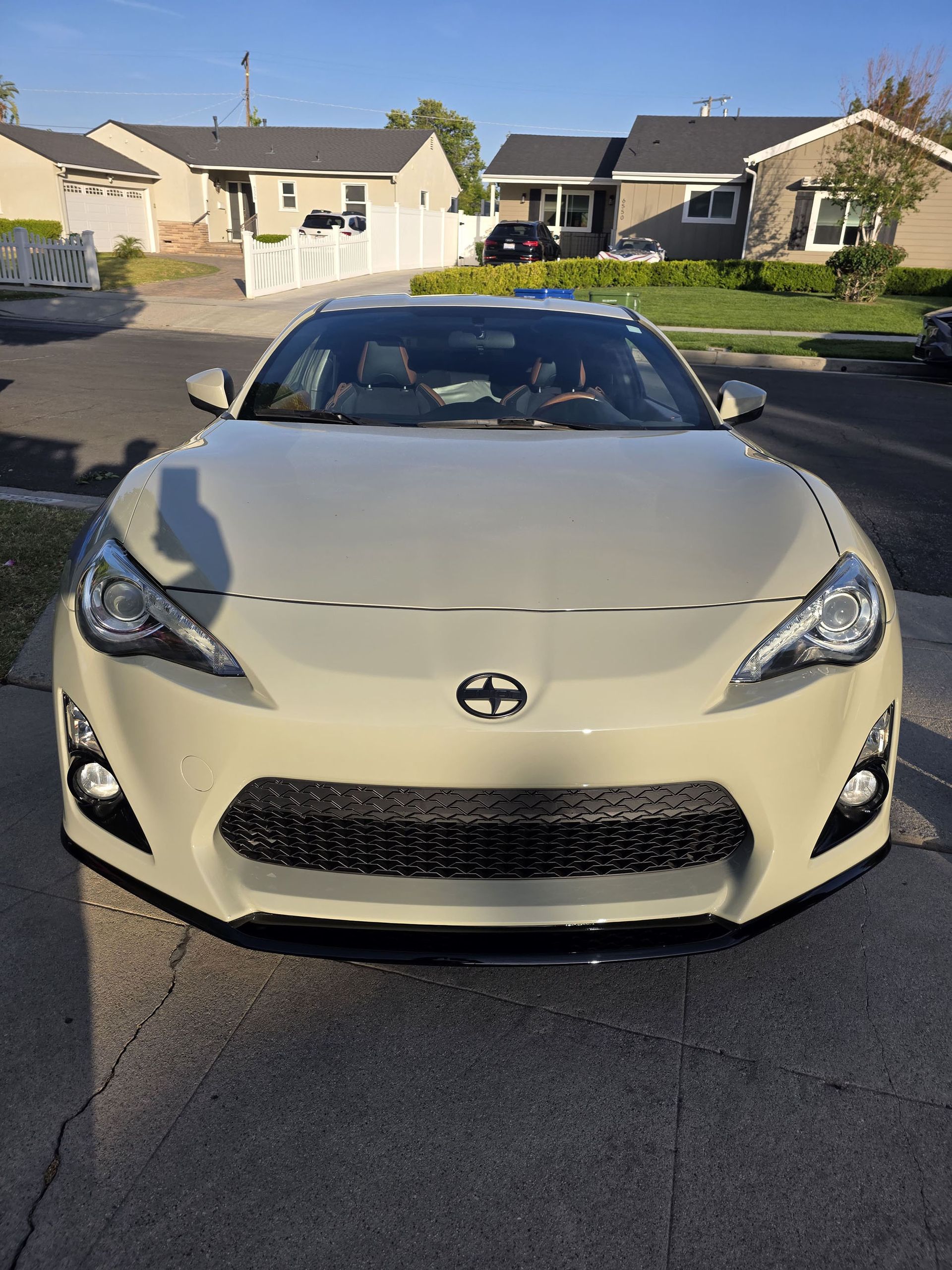 White sports car parked on a suburban street in front of houses at sunset
