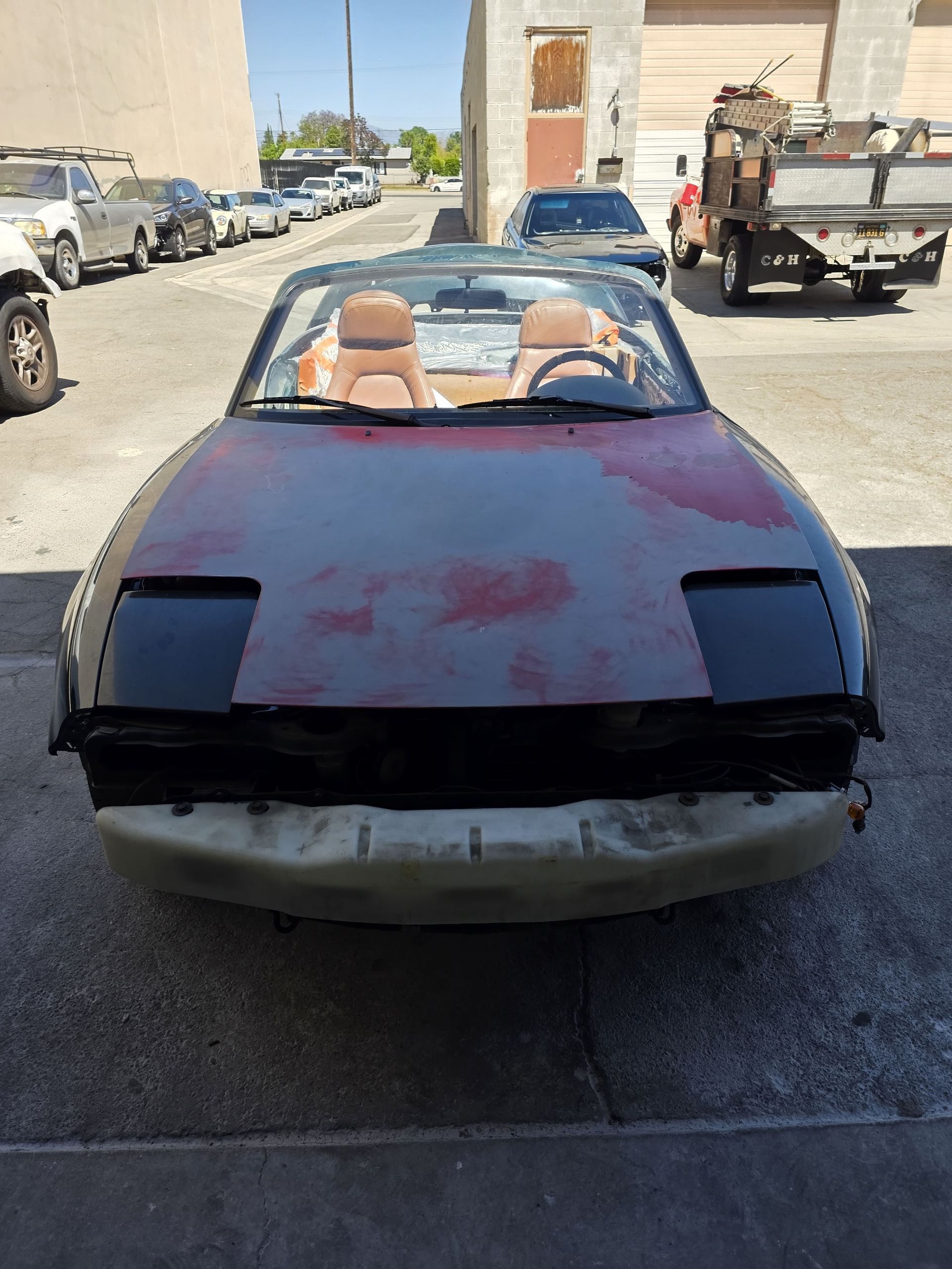 Pink convertible with blacked-out headlights parked on a street, tan seats visible inside.