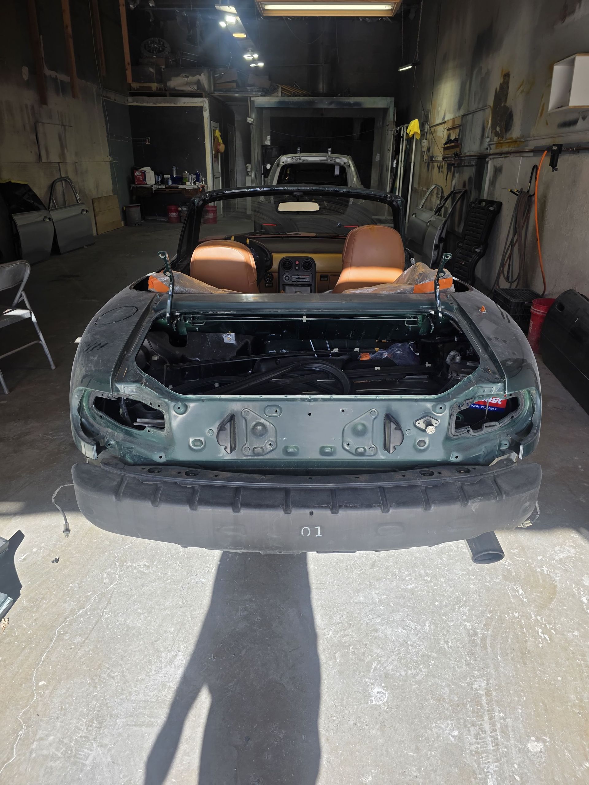 Damaged gray convertible sports car in a garage with tan seats exposed and front bumper missing