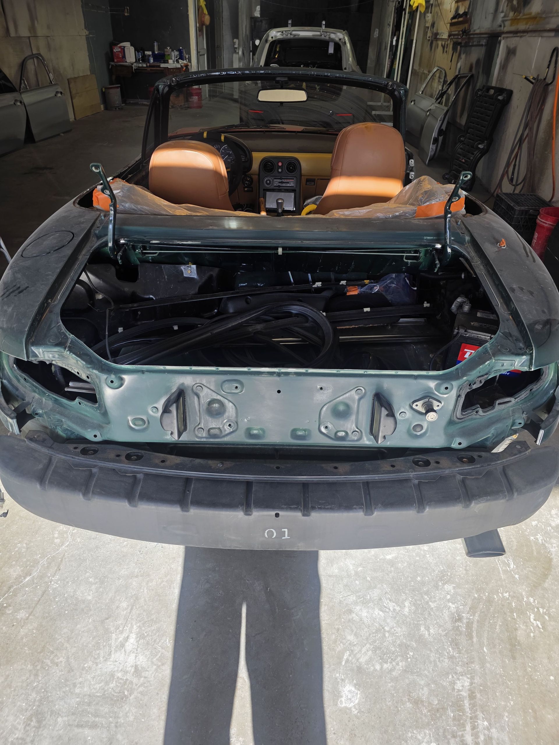 Convertible sports car with hood open in a garage, showing tan seats and exposed engine bay.