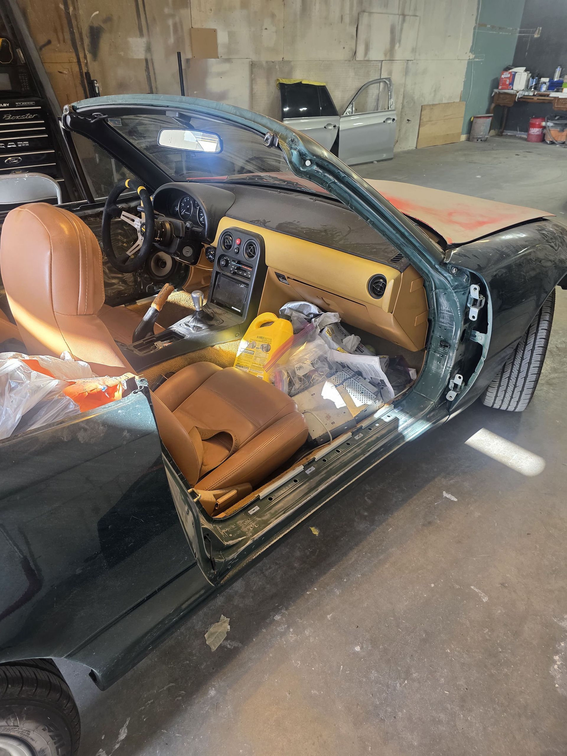 Black convertible car with tan interior in a garage, windshield shattered and driver’s door open with debris inside