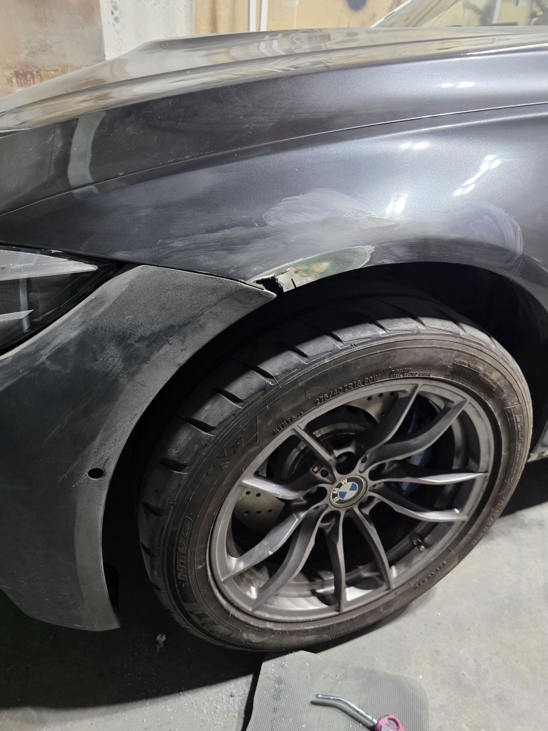 Close-up of a black car’s rear wheel and fender with visible body damage and a detached bumper.
