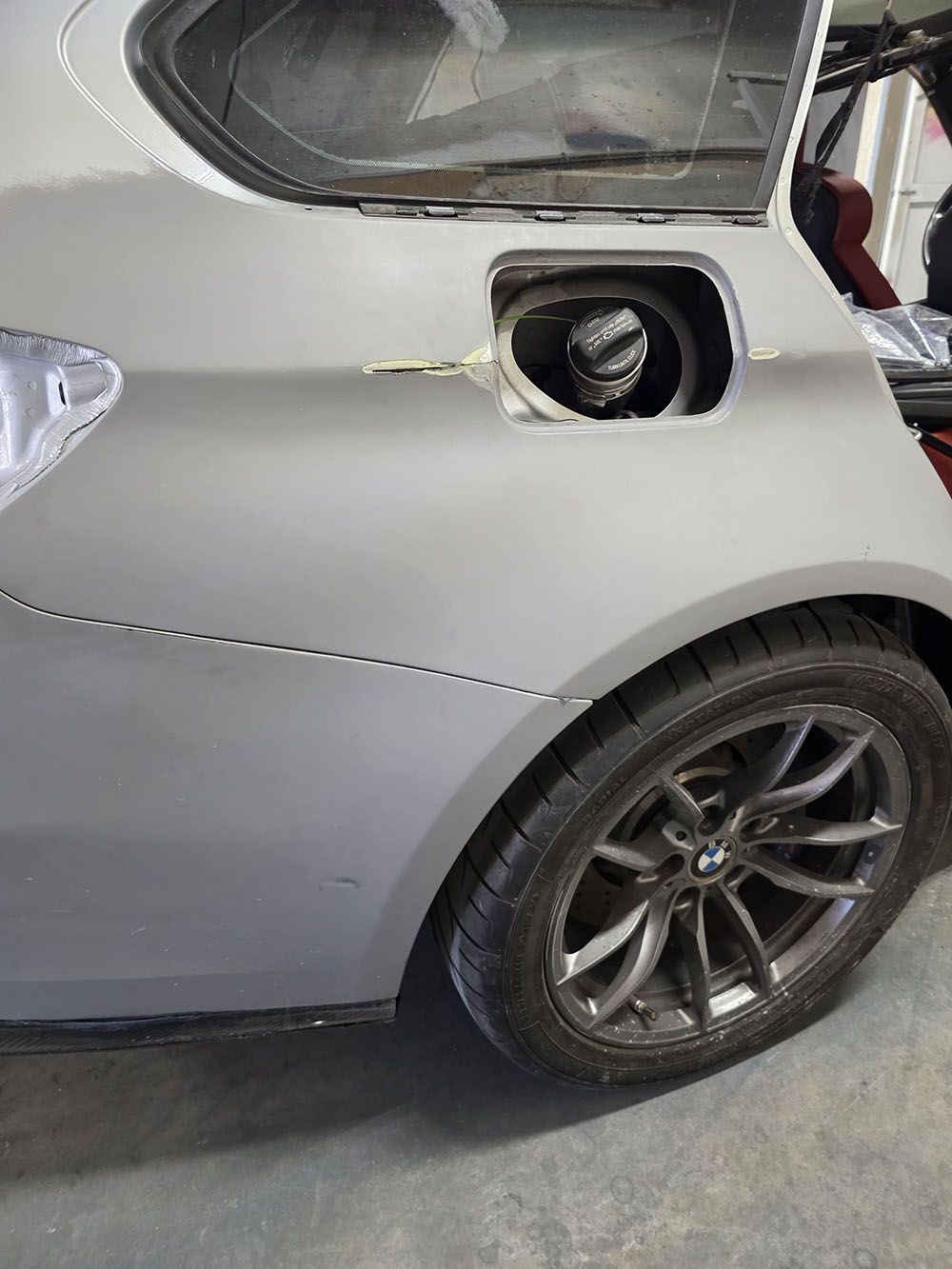 Silver sports car with rear side damage and open fuel door, parked indoors with missing fuel cap.