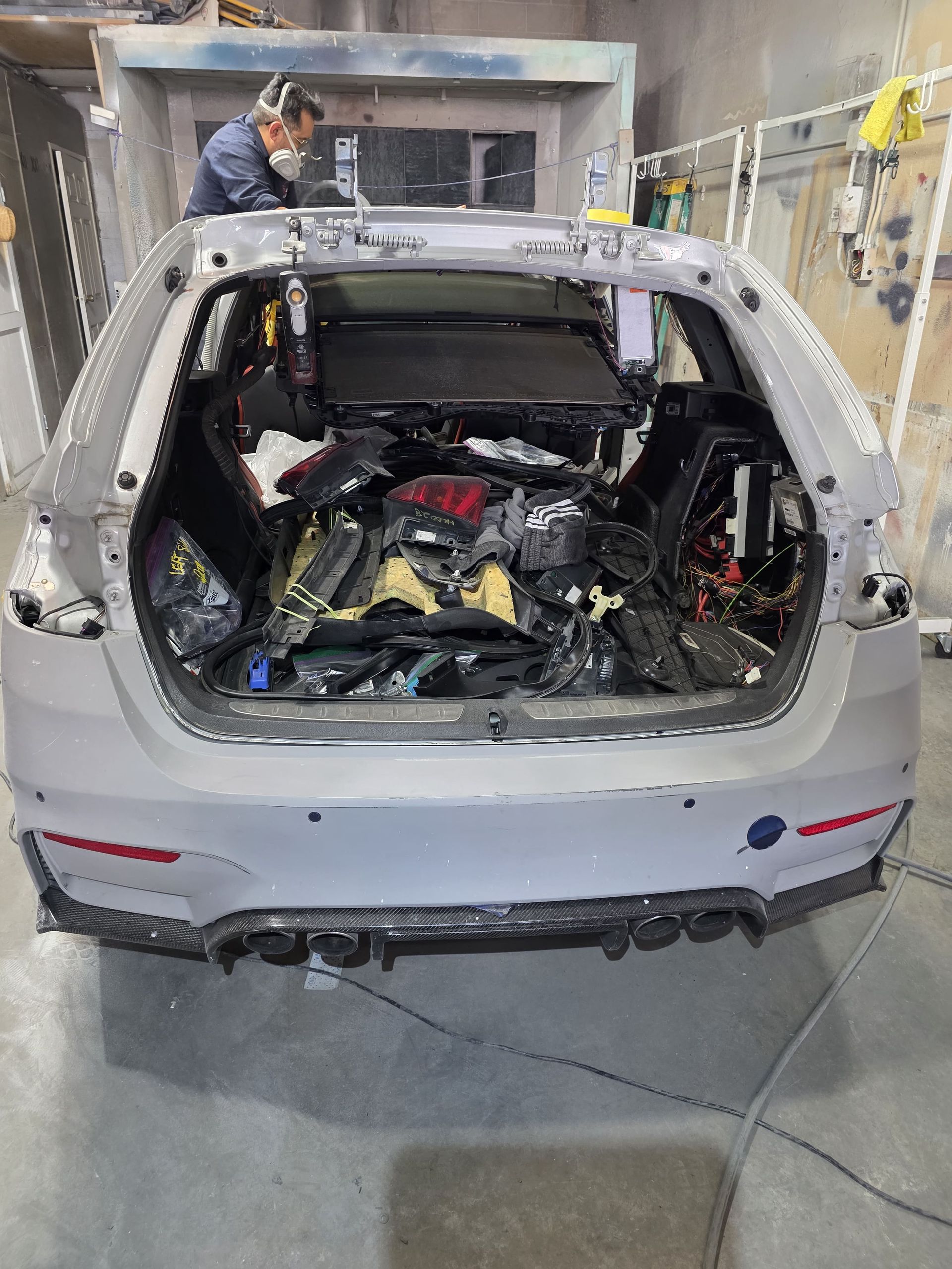 Car trunk packed with machinery and tools in an industrial workshop; a worker stands nearby.