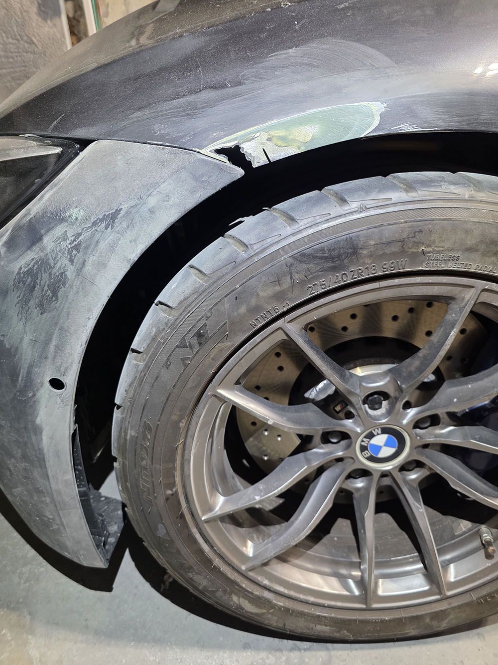 Damaged black car front wheel and fender, with scuffed rim and cracked body panel.