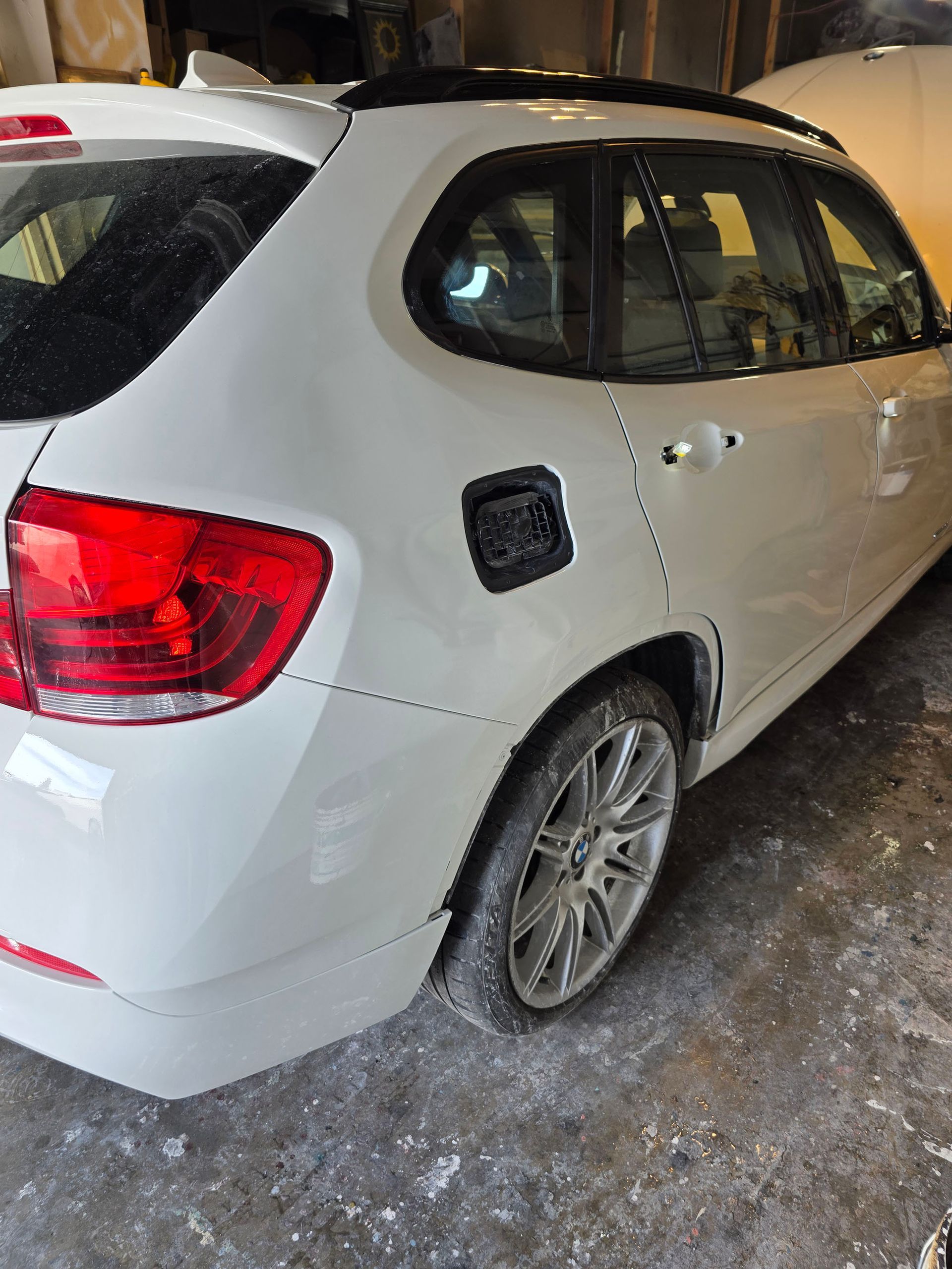 White SUV parked in a garage with a damaged rear side panel near the fuel cap