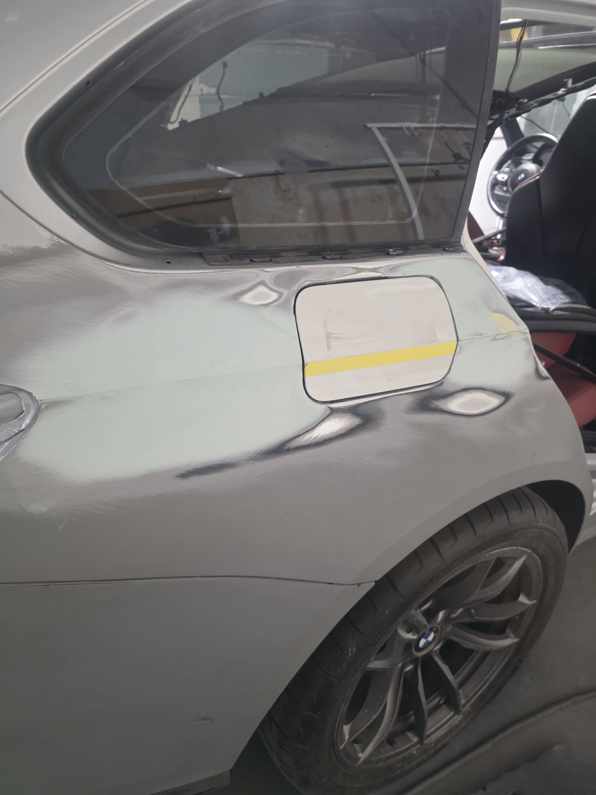 Gray sports car in a garage, rear side view with the fuel door open and taped over.