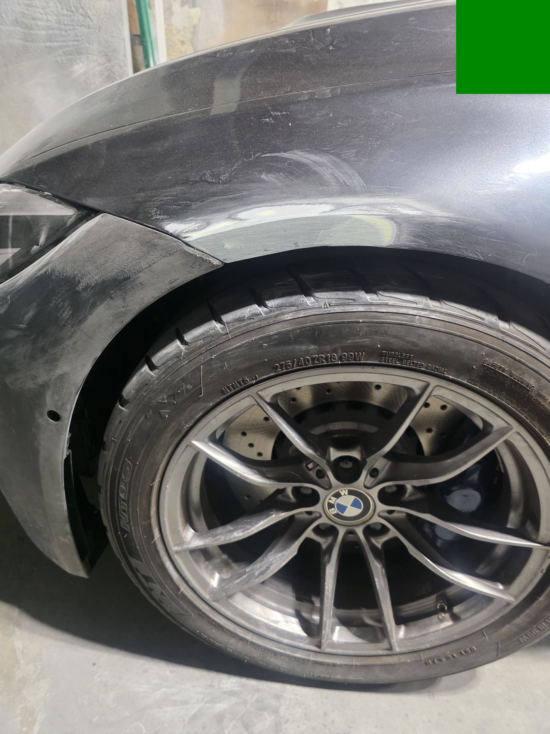 Close-up of a dirty black BMW wheel and front fender with visible scuffs.