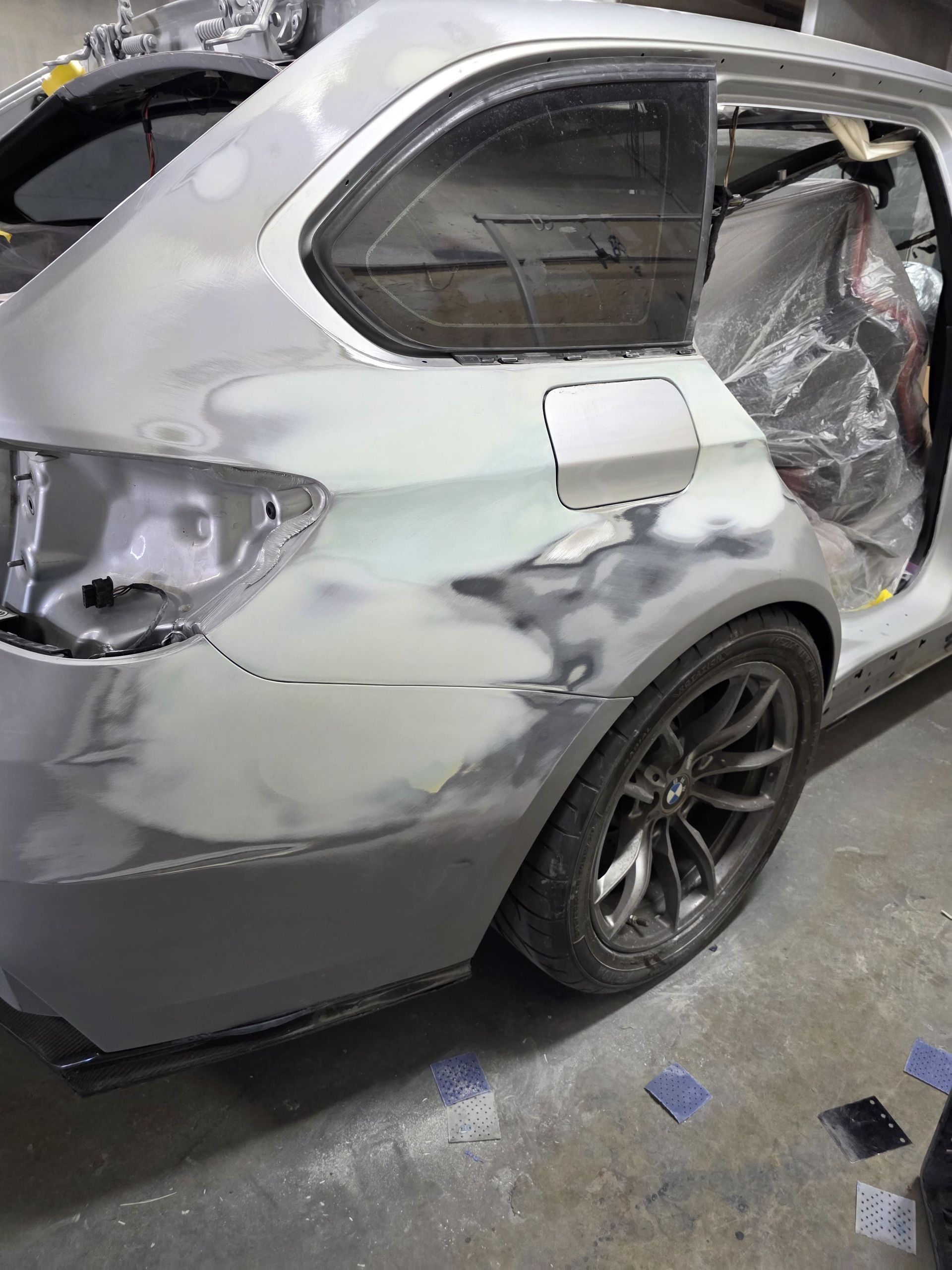Rear side of a silver car in a body shop, with fresh body filler and sanded repair panels exposed