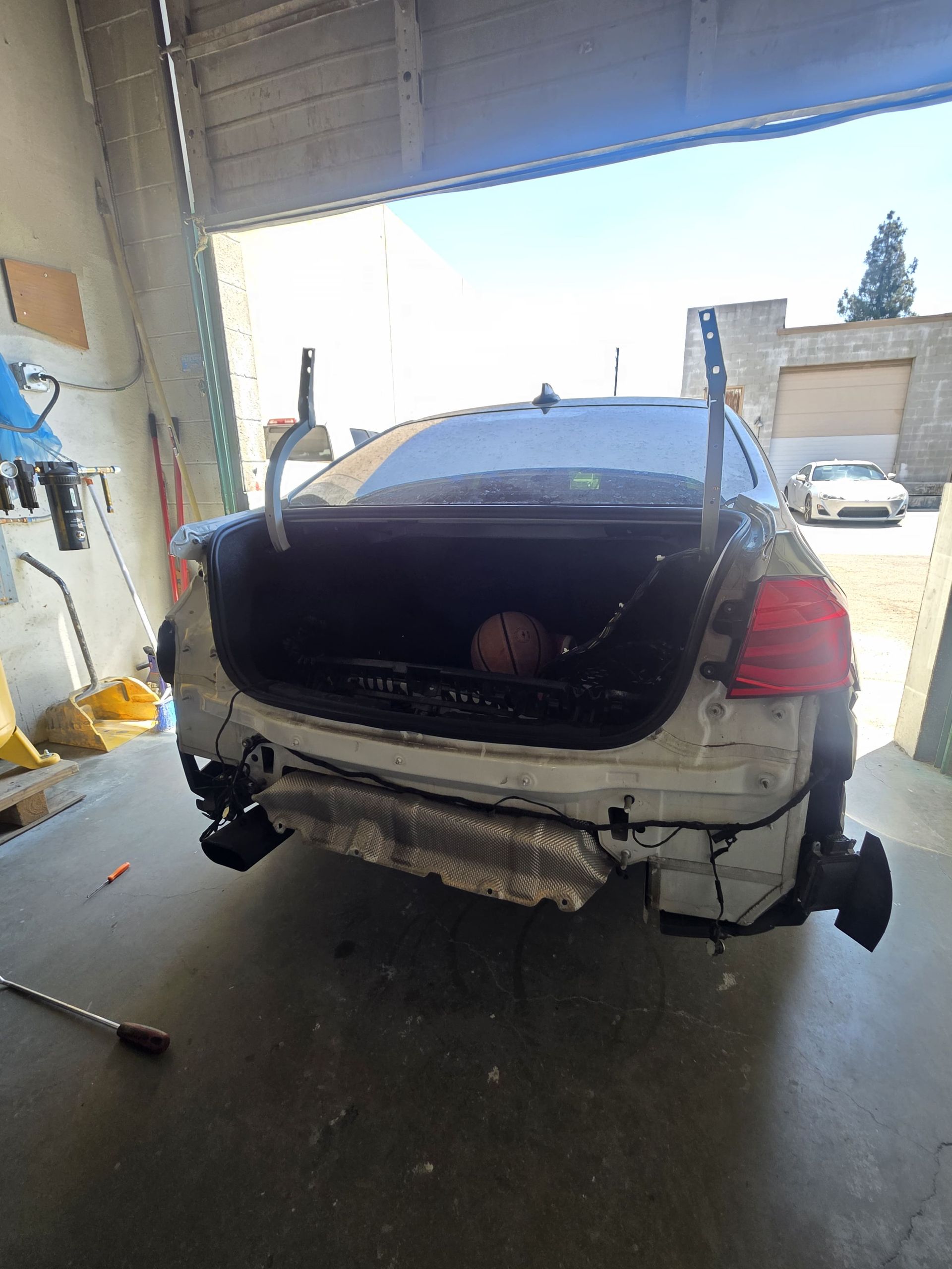 Damaged silver pickup truck parked inside a garage with its rear hatch open and bumper hanging off