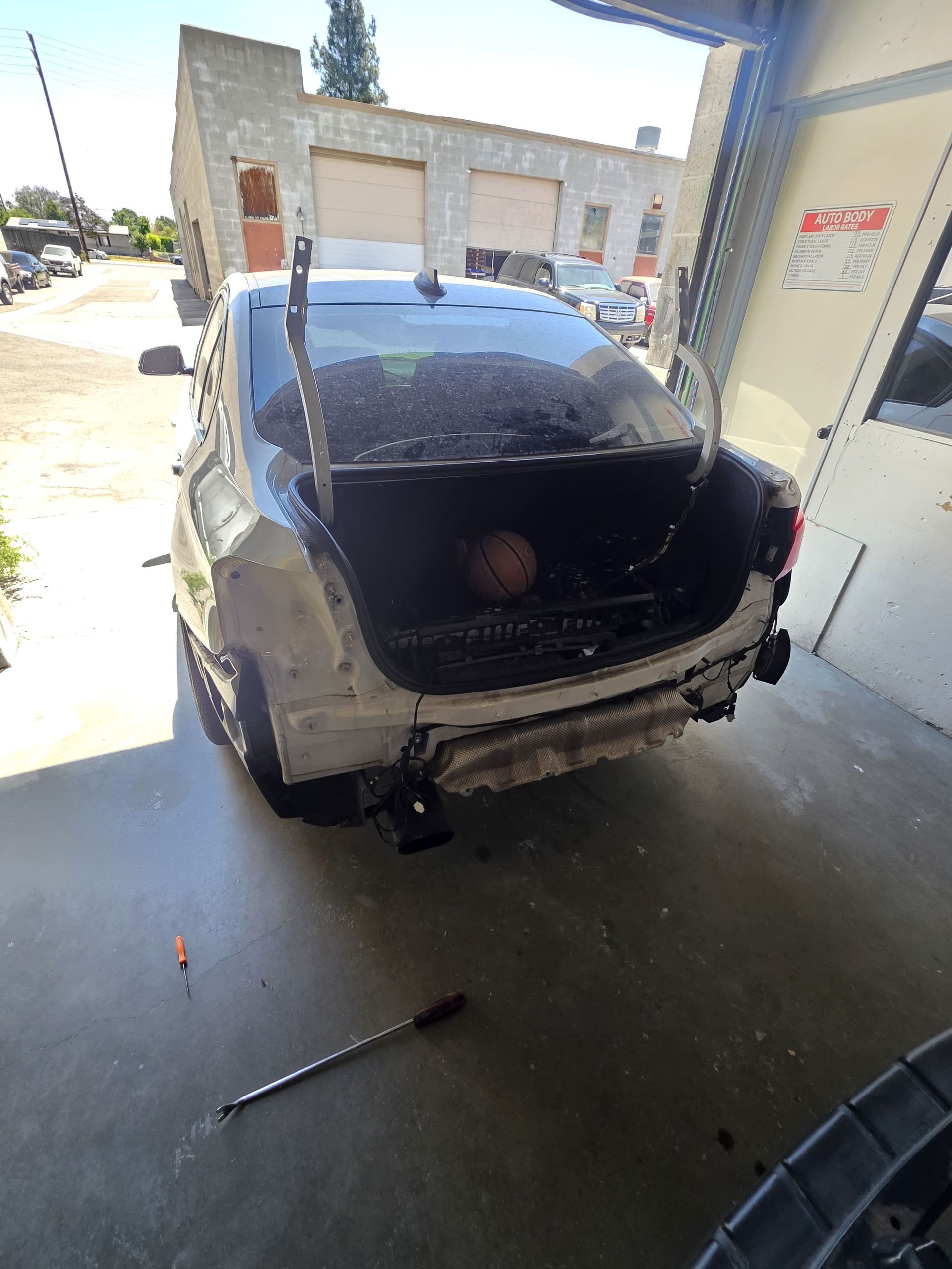 Silver car with open hatch in a garage bay, rear bumper damaged and trunk empty.