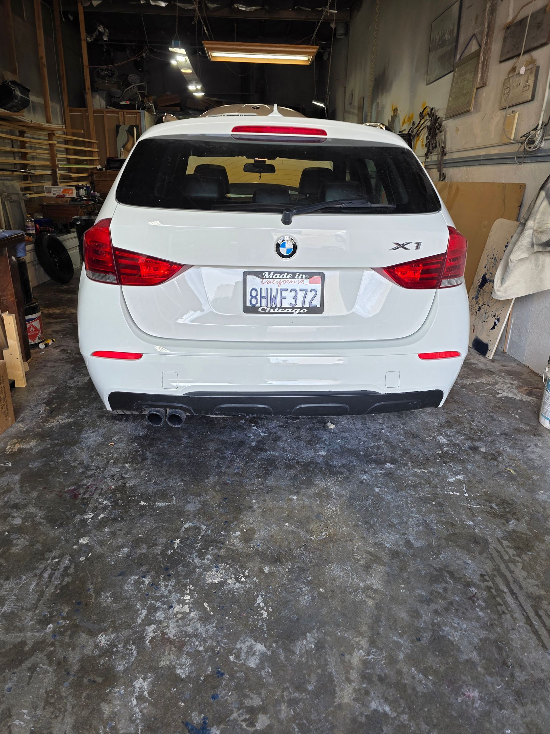 White BMW SUV parked inside a cluttered garage, rear view.