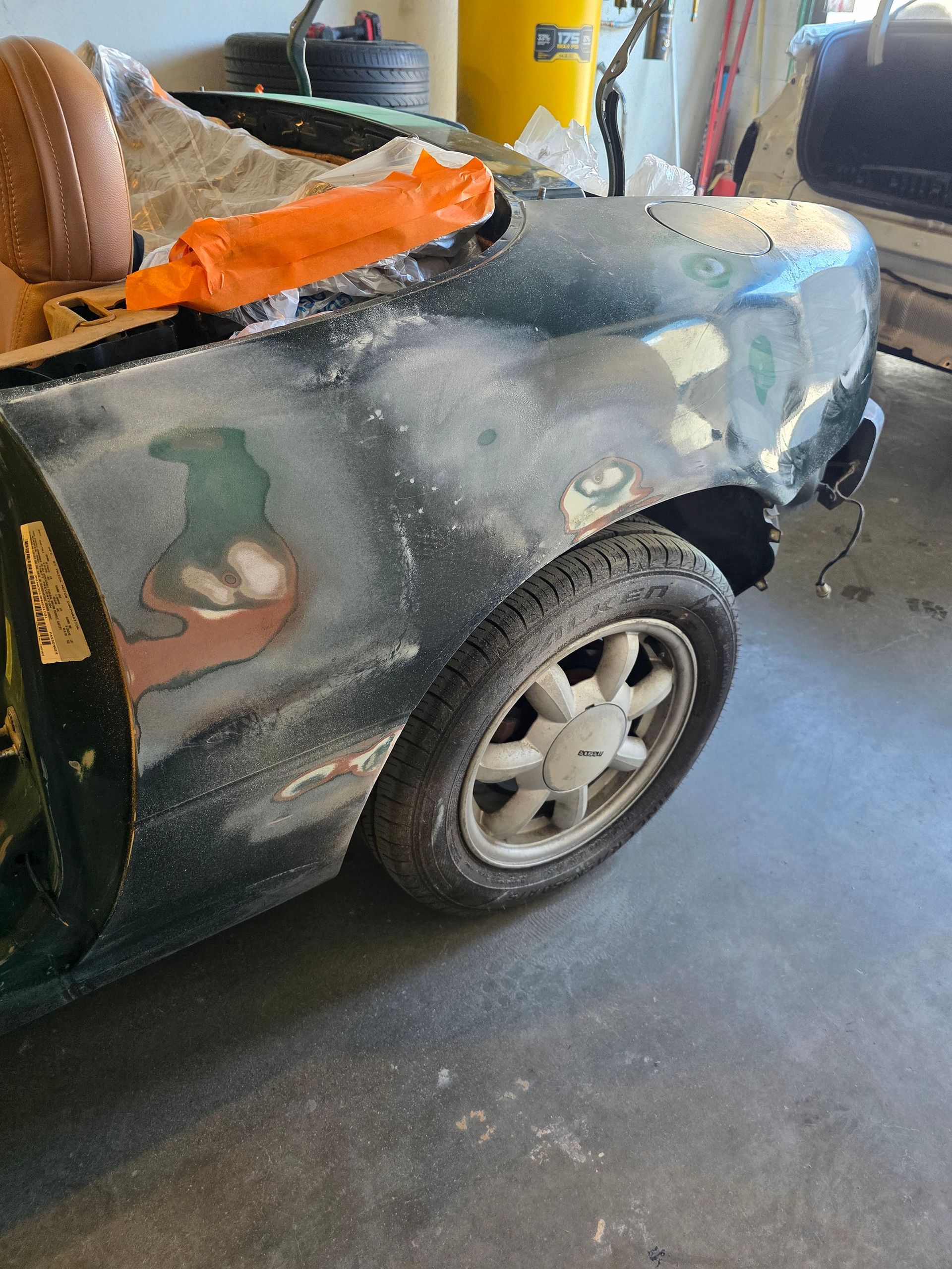 A small car-shaped vehicle shell in a garage, painted gray with orange tape and patches visible.