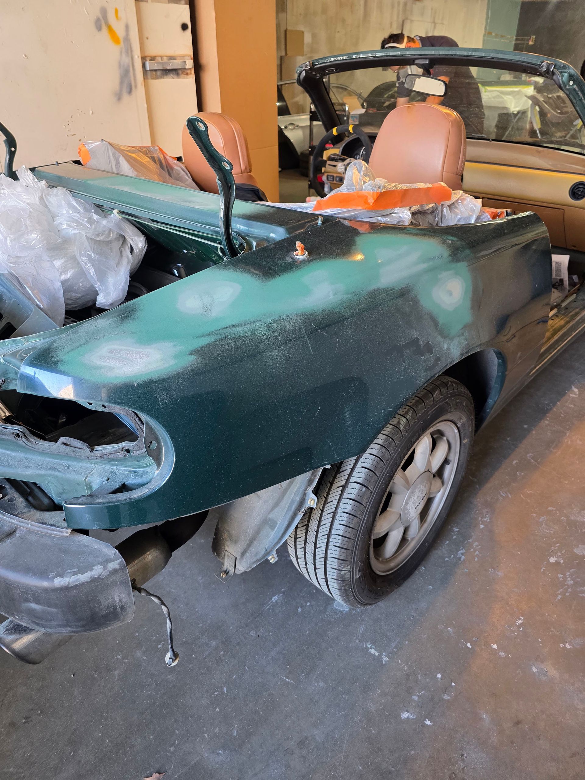 Damaged green convertible car in a garage, with a missing front wheel and worn interior