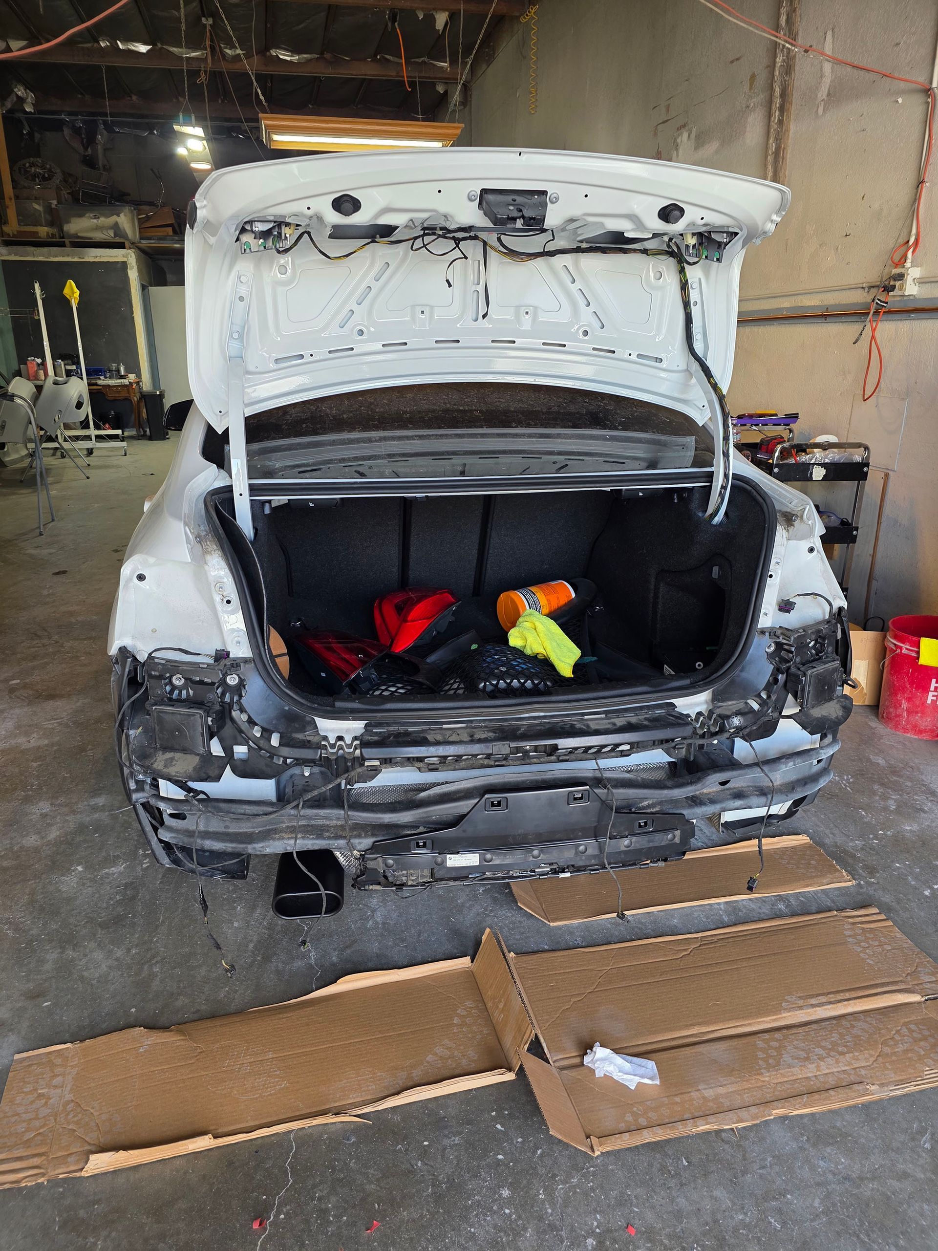 Damaged white car in a garage with open hatch and cardboard on the floor