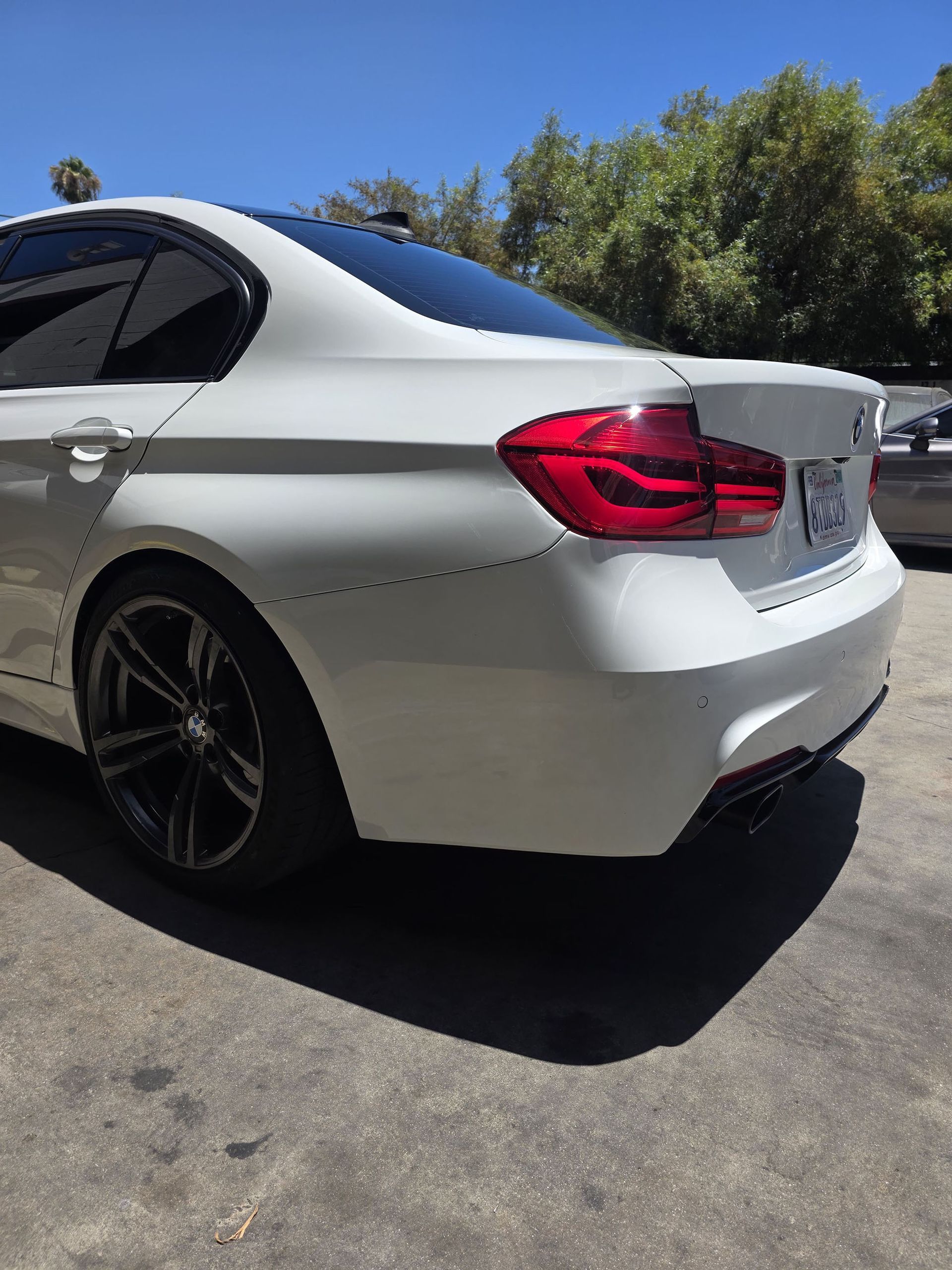 Silver sedan parked outdoors on a sunny street, rear side view with red taillights and black rims