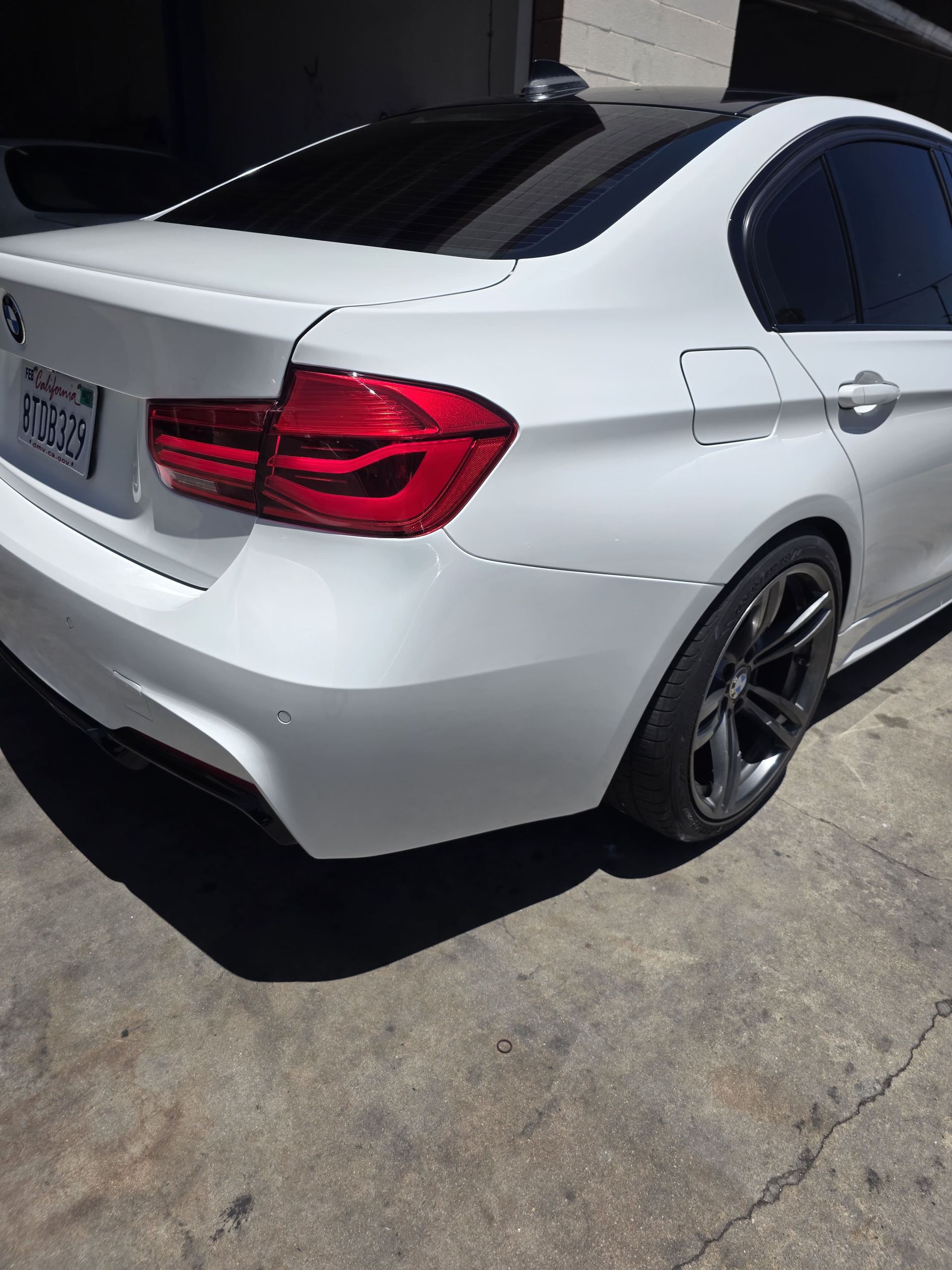 White sedan parked in a driveway, rear three-quarter view, with dark tinted windows and black wheels