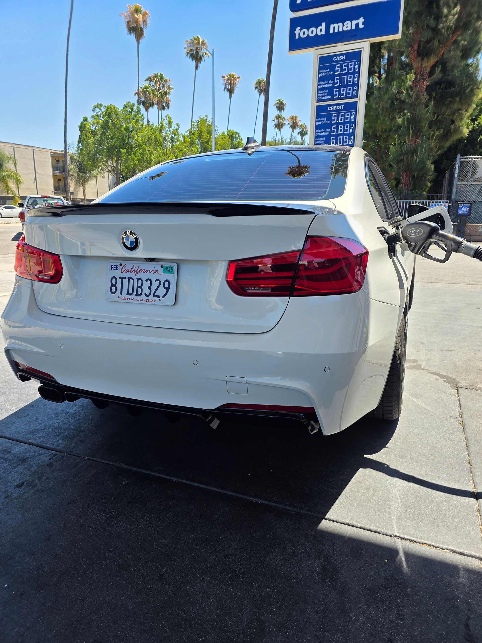 White BMW sedan parked on a sunny street near a blue sign and palm trees