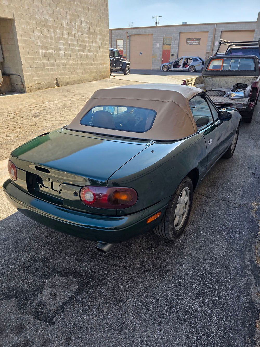 Green convertible parked in a lot beside a stone wall, with another car behind it.