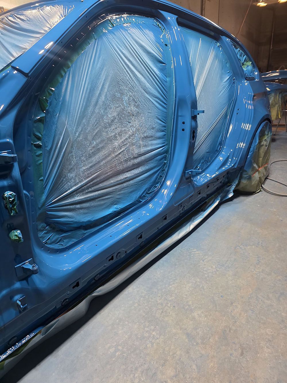 Blue vehicle door covered in protective plastic sheeting inside a workshop