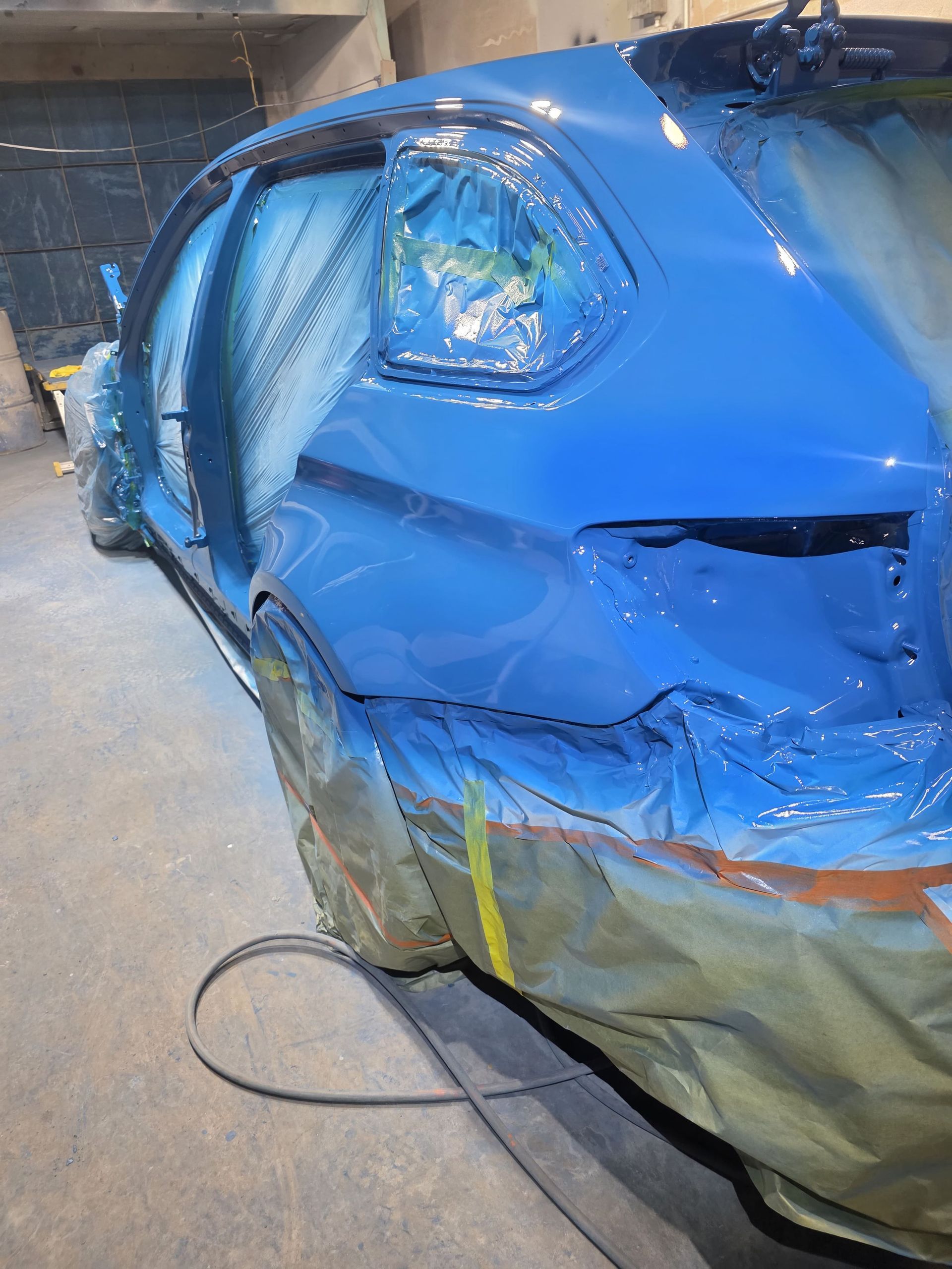 Blue car covered in masking tape and plastic in a paint booth during body repair