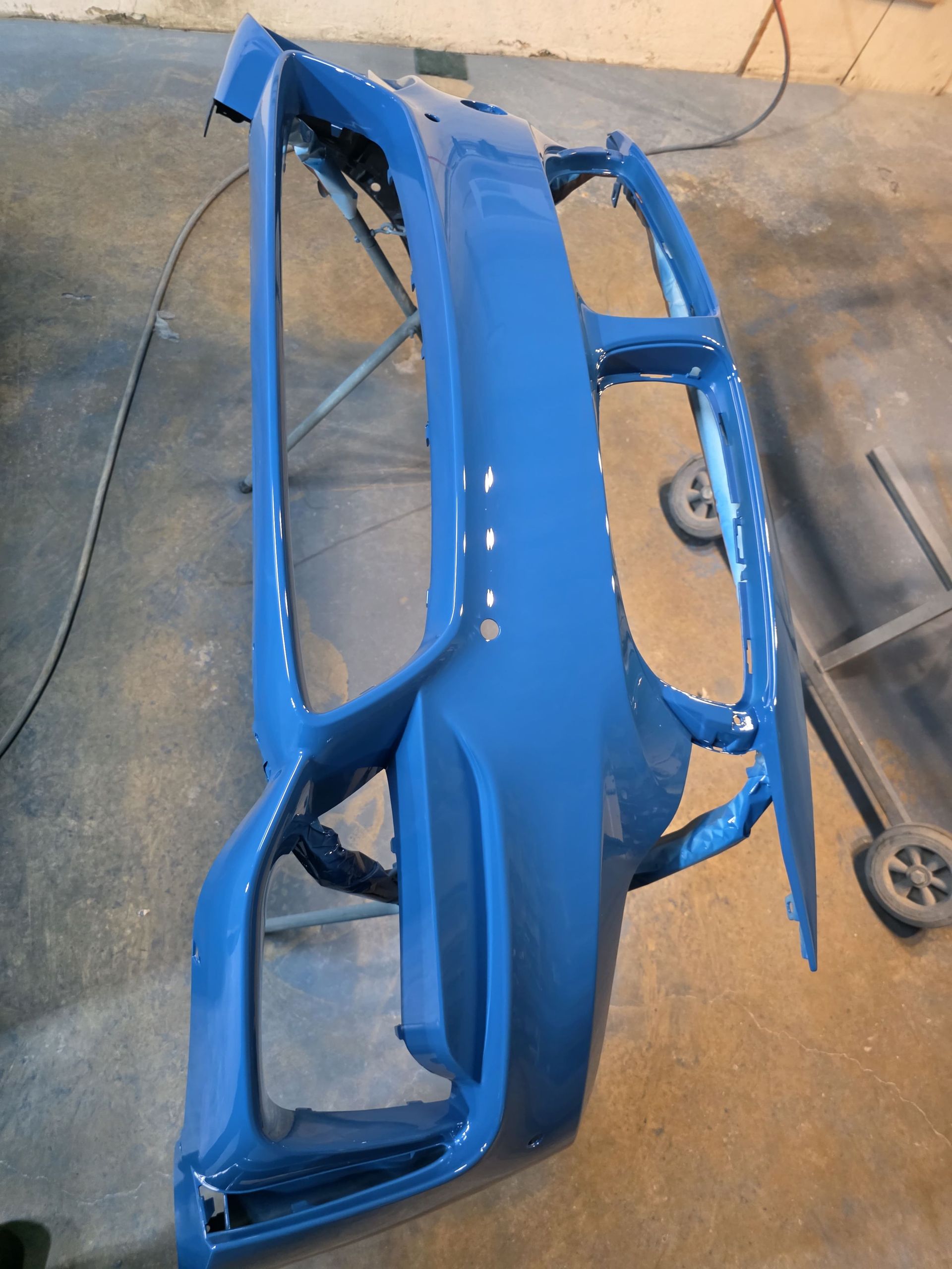 Blue car bumper and body panel resting on a concrete floor in a workshop