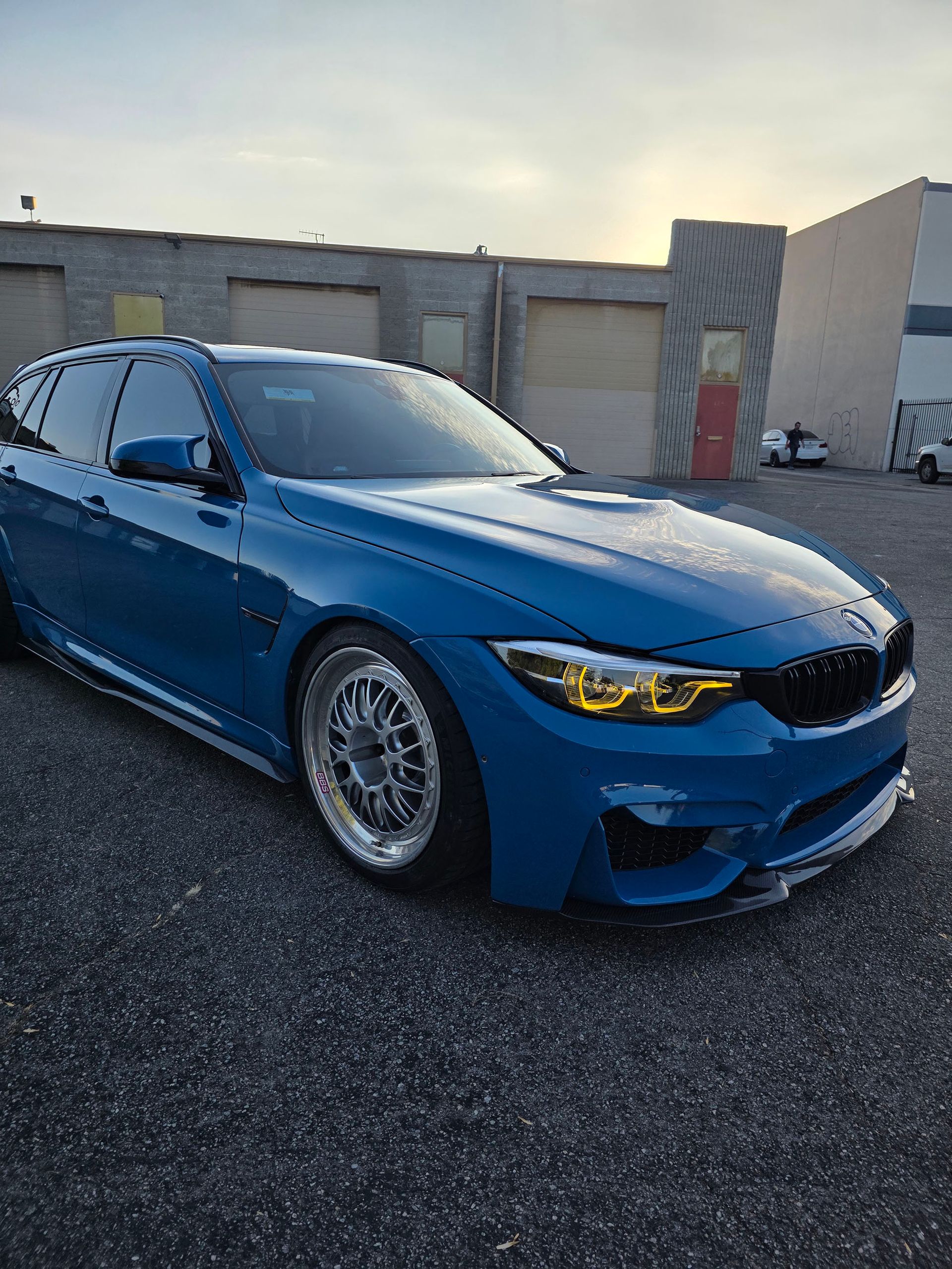 Blue sports sedan parked outdoors in front of concrete buildings, with yellow headlights and tinted windows