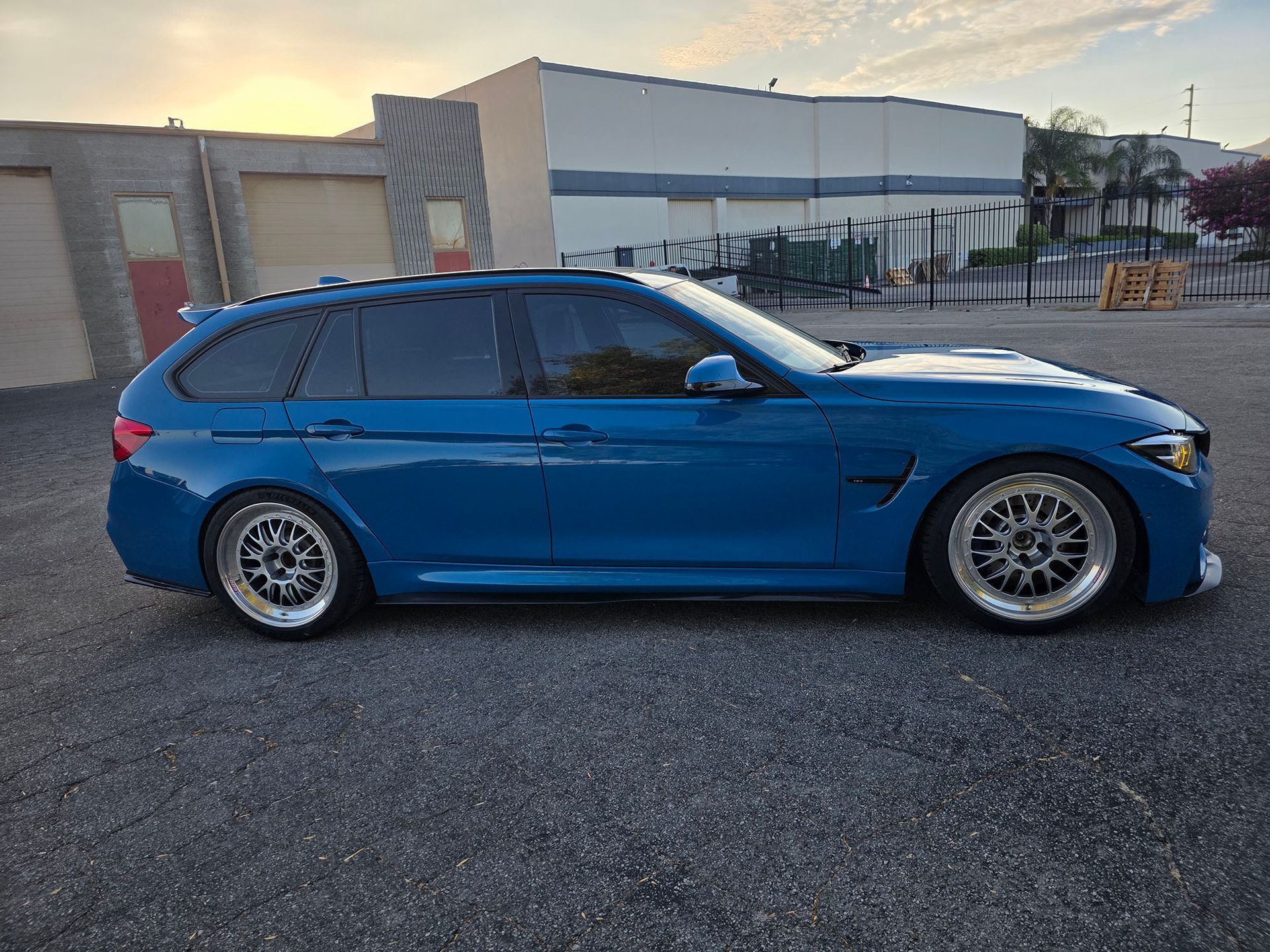 Blue sports wagon parked on asphalt in front of a building at sunset