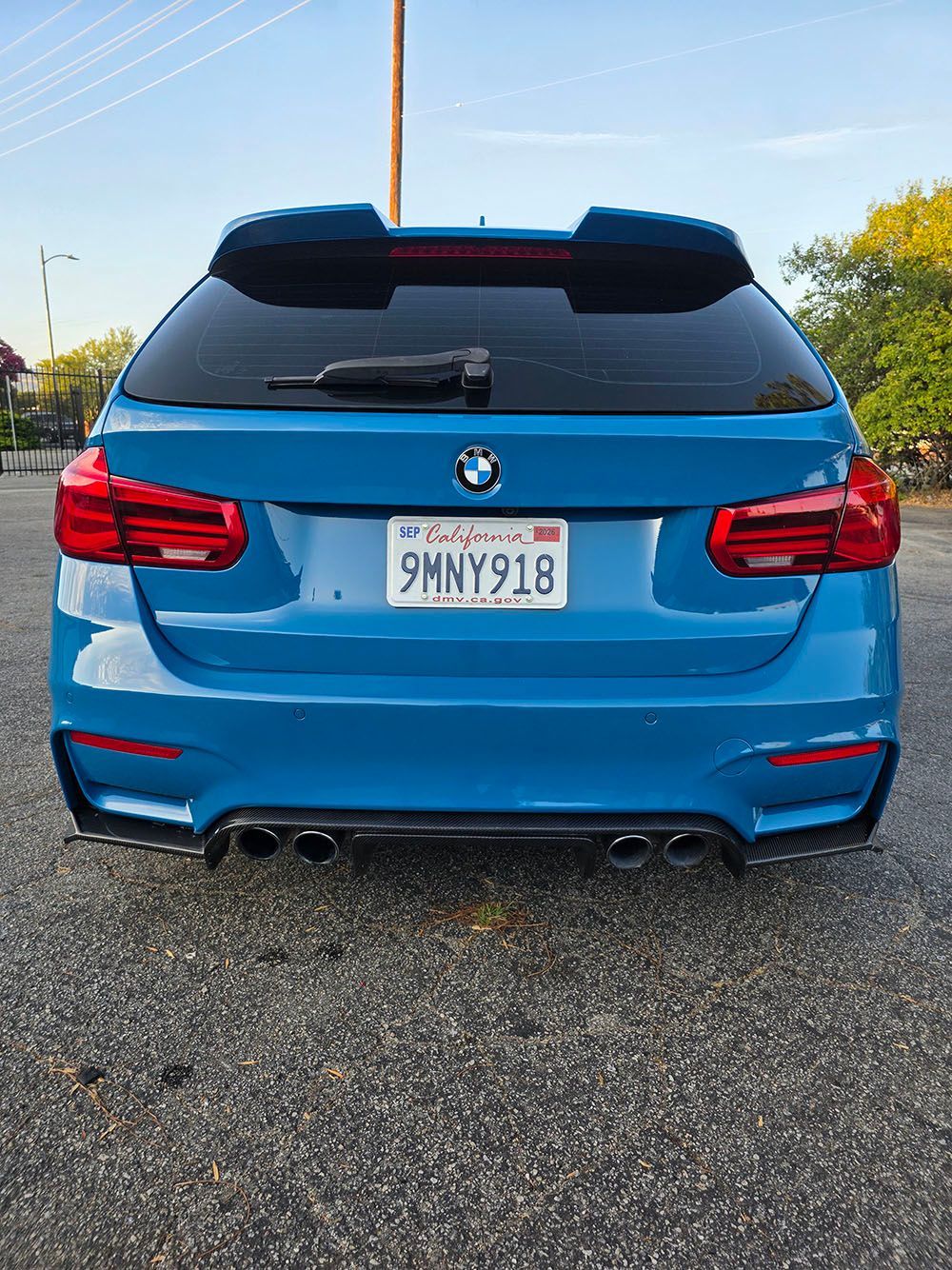 Blue BMW SUV seen from the rear in a parking lot, with red taillights and a roof spoiler.