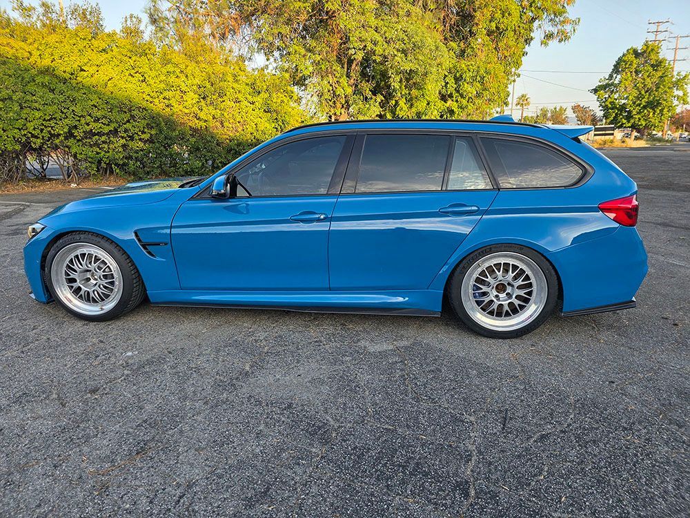 Blue sedan parked on gravel beside a hedge, side view.