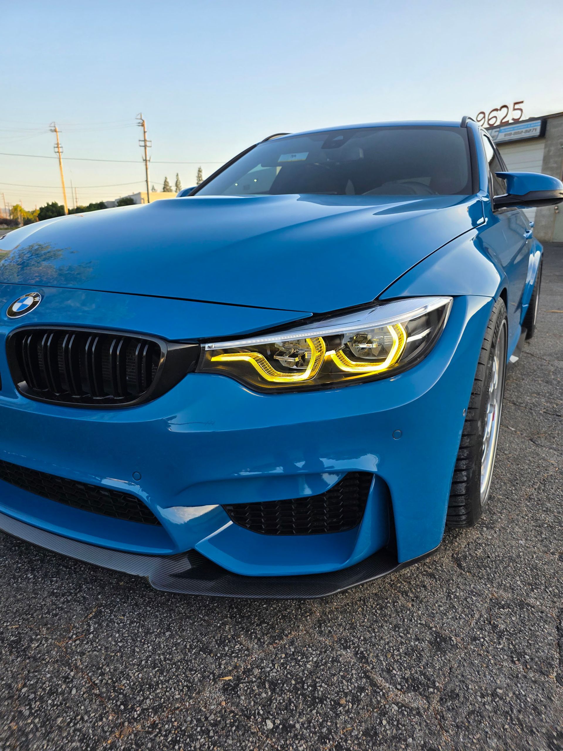 Blue BMW with yellow headlights parked outdoors at sunset
