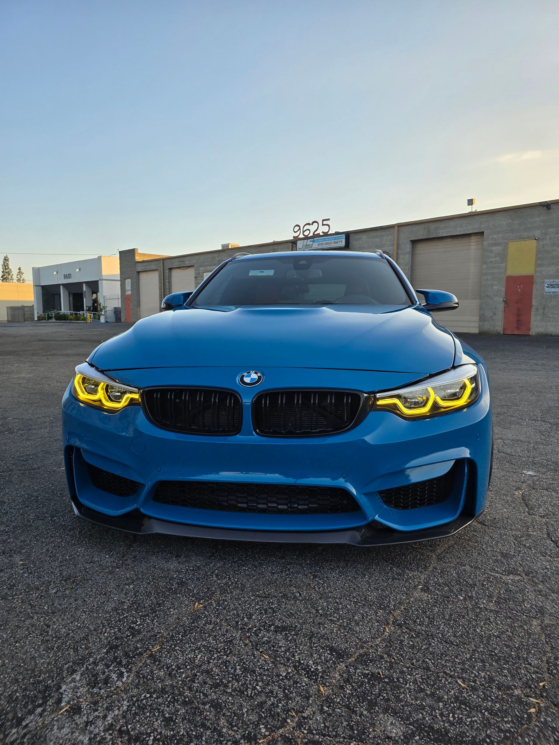 Blue BMW sedan parked in front of an industrial building at sunset