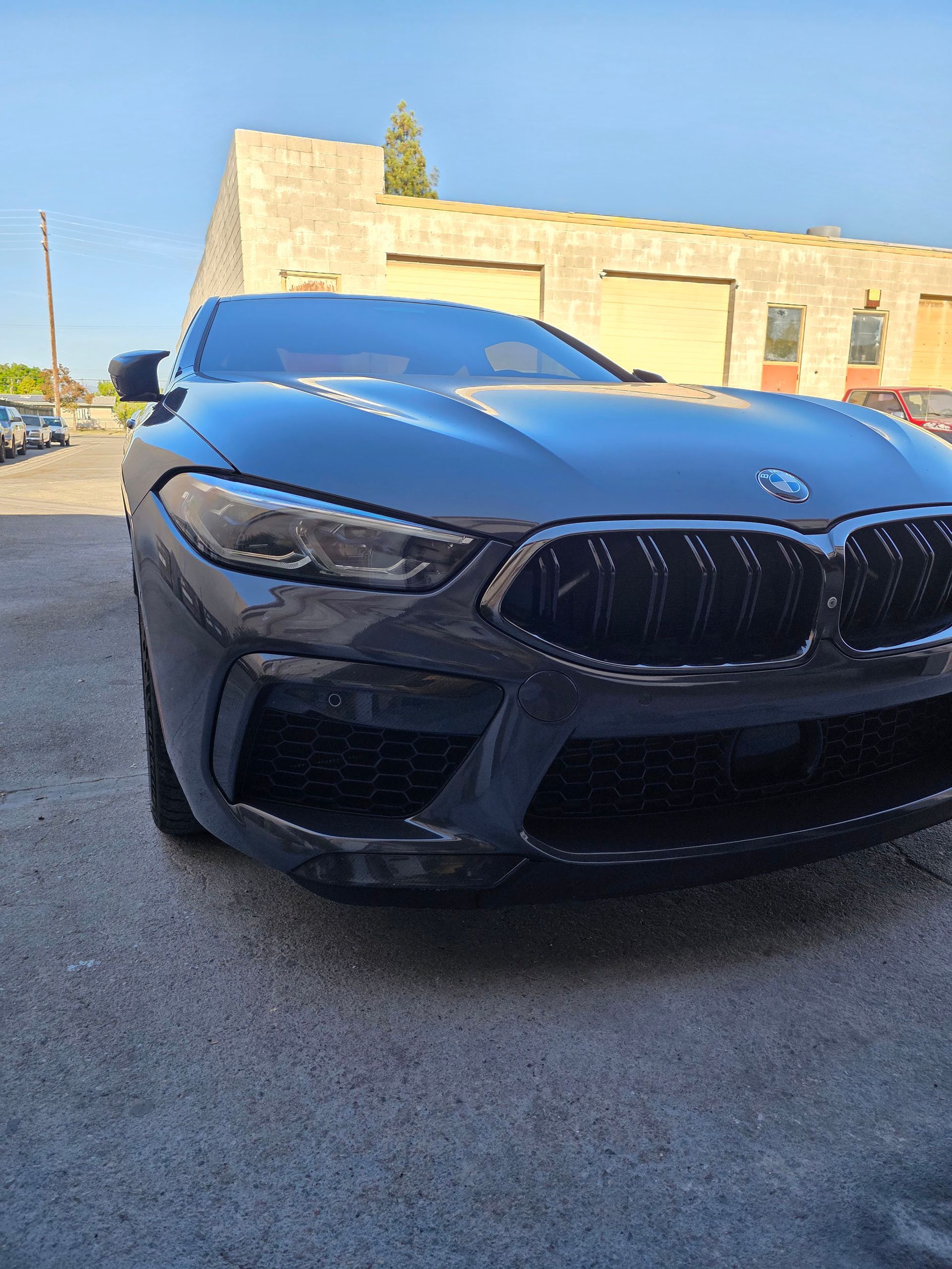 Black BMW sports car parked in a driveway, front view with sunlit building in the background