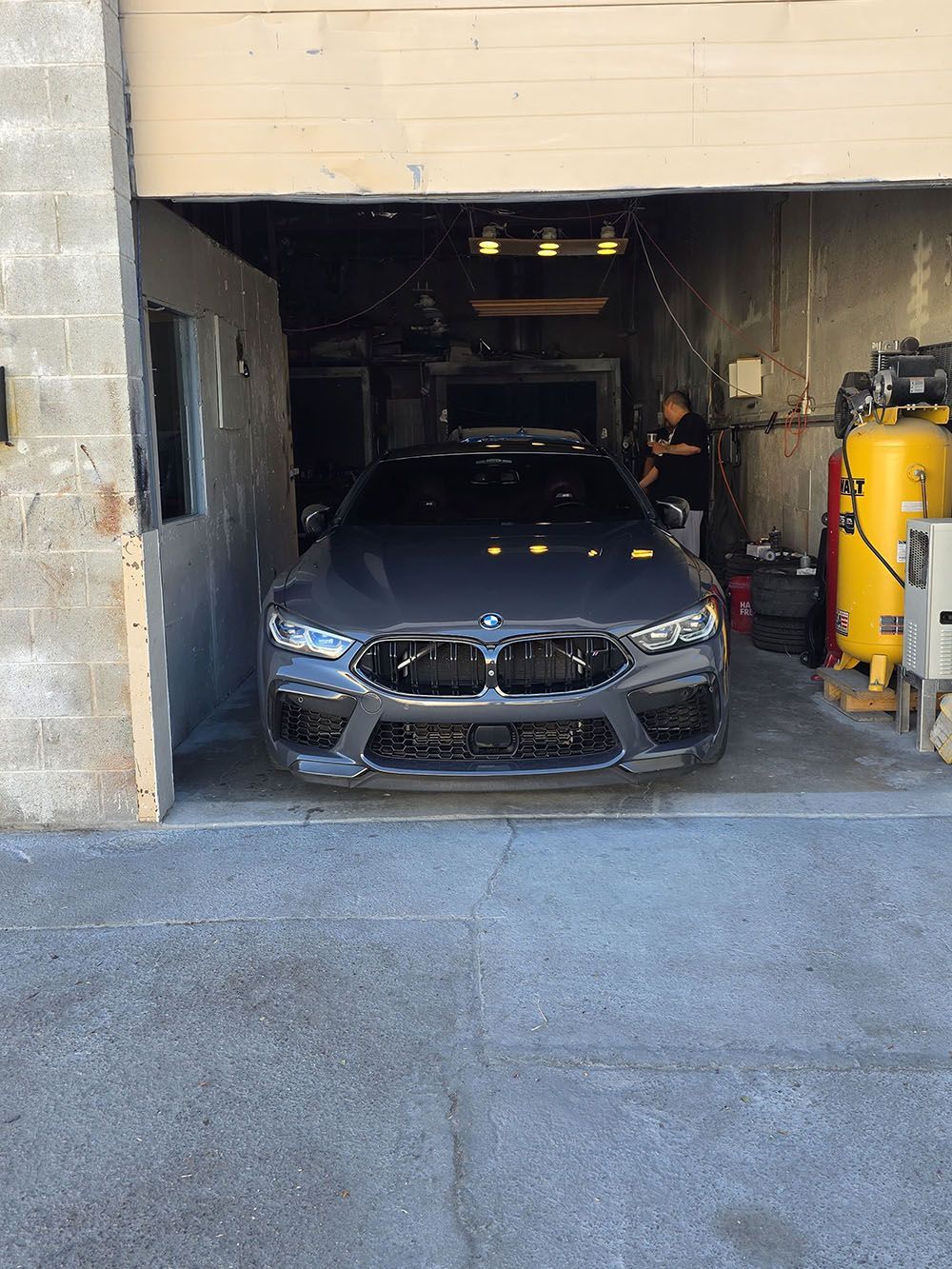 Black BMW parked in a garage entrance with yellow tanks on the right and a concrete driveway outside