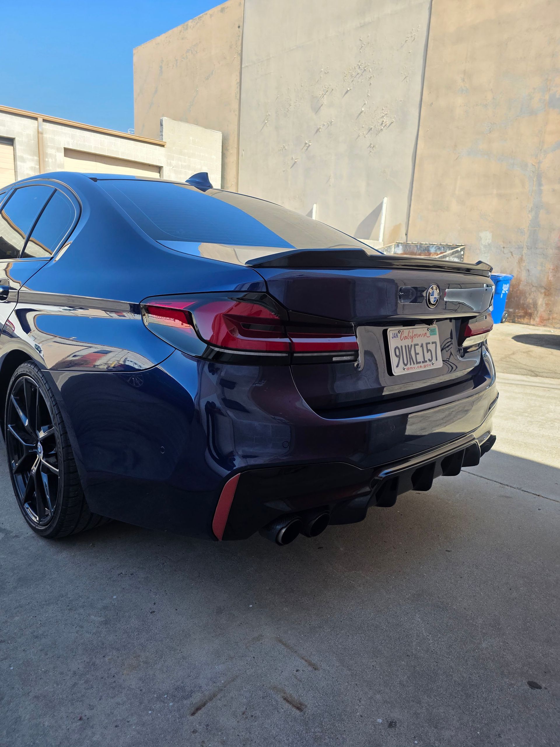 Black BMW SUV parked outdoors beside a concrete wall, rear view with tinted taillights.