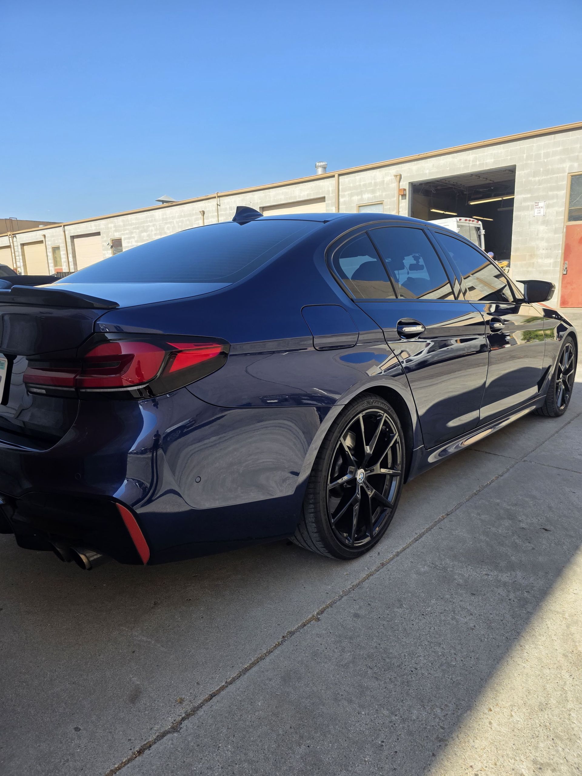 Dark blue sports sedan with black rims parked beside beige industrial buildings.